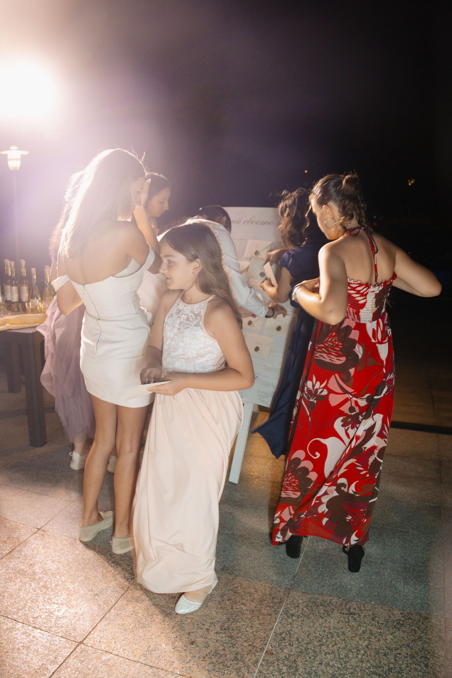 Wedding guests in formal attire dance energetically at an outdoor nighttime wedding reception.