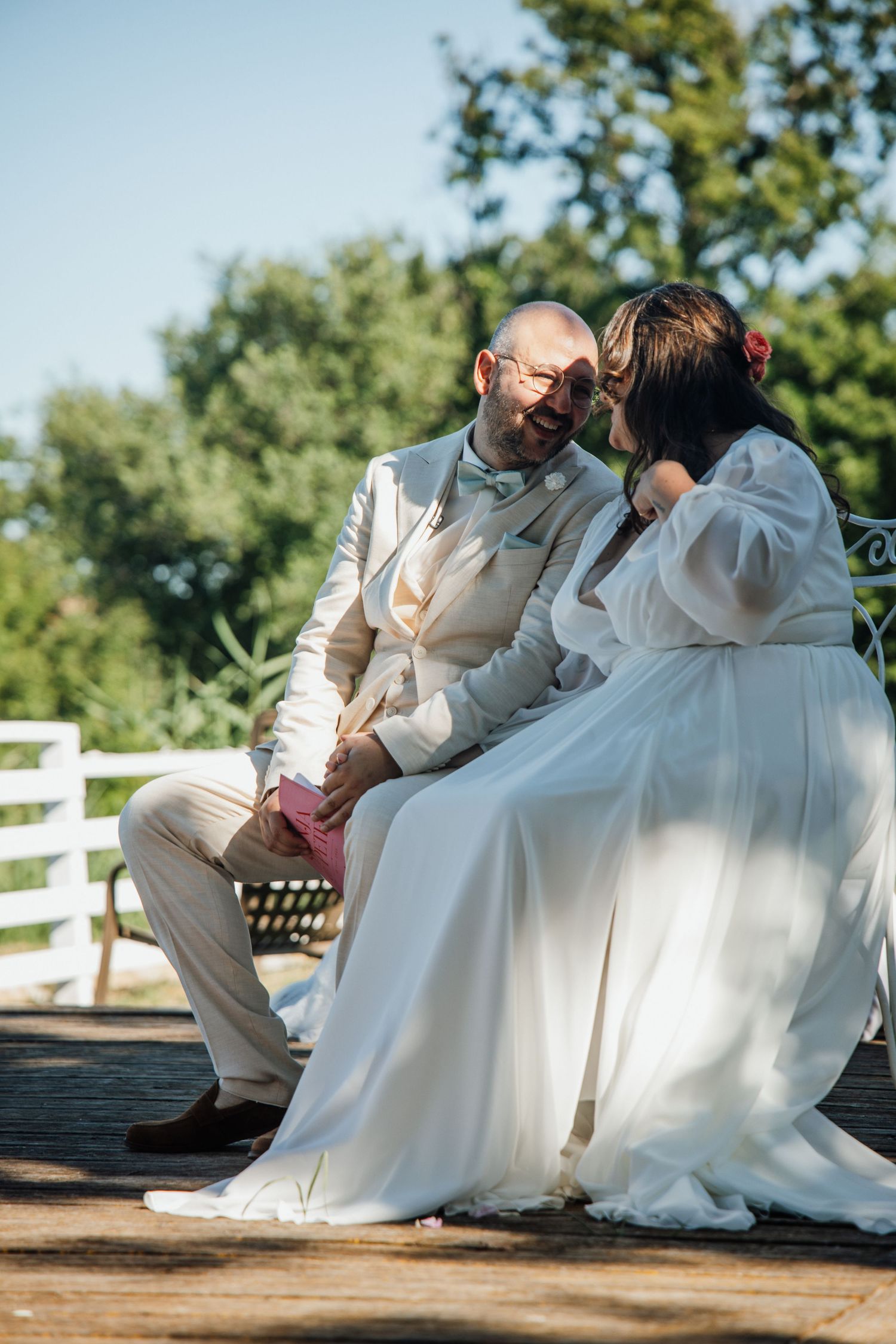 Bride and groom sitting together on a bench in a sunny garden during their wedding day.