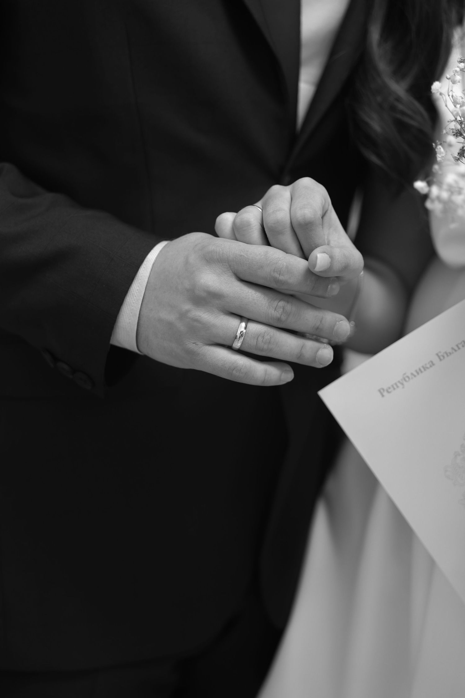 Black and white photo of newlyweds holding hands, groom wearing wedding ring, holding Pennsylvania marriage certificate.