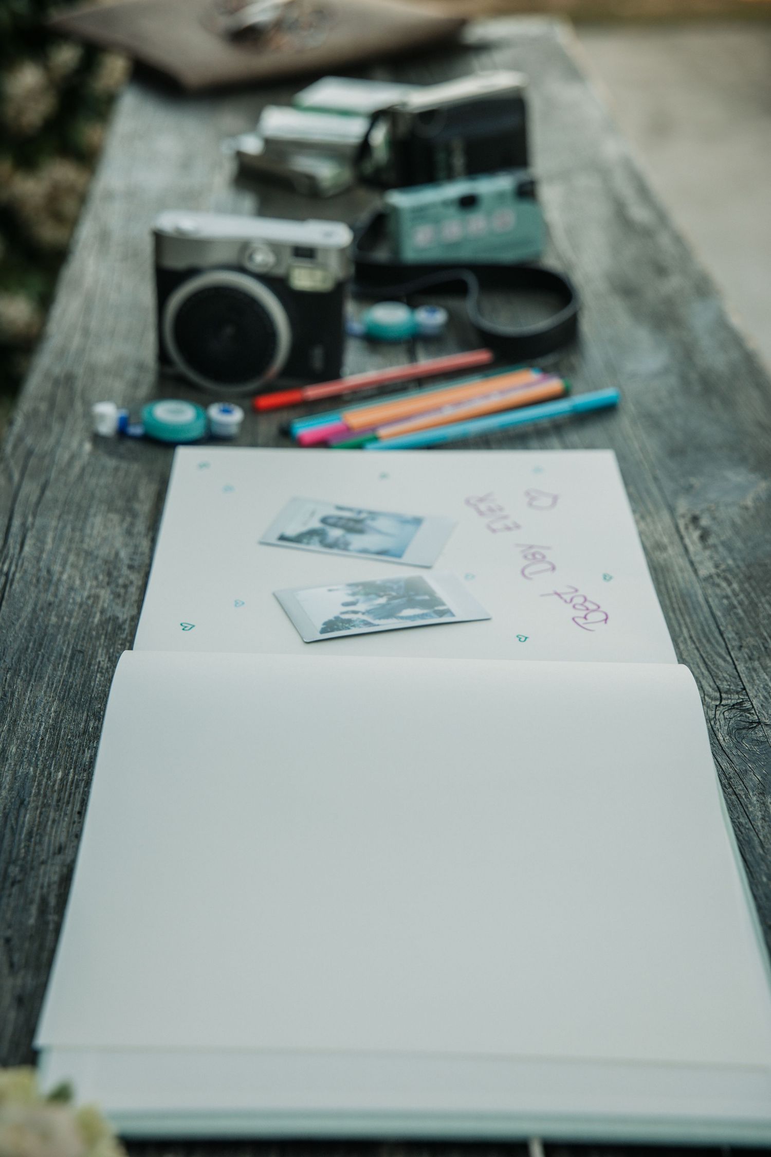 Wedding guest book open on wooden table with vintage cameras and colorful markers.