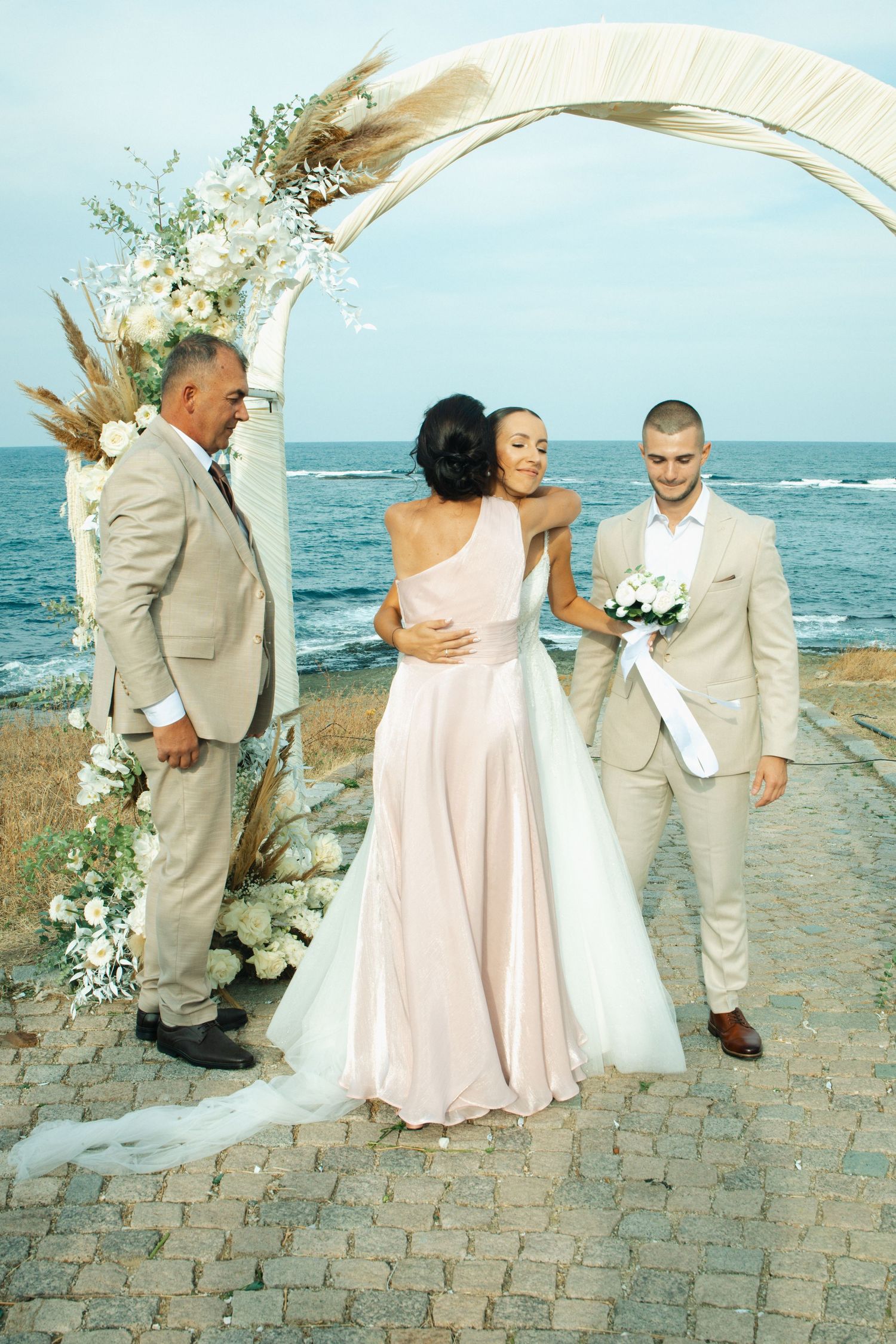 Couple exchanges vows at beach wedding ceremony under floral arch with ocean backdrop.