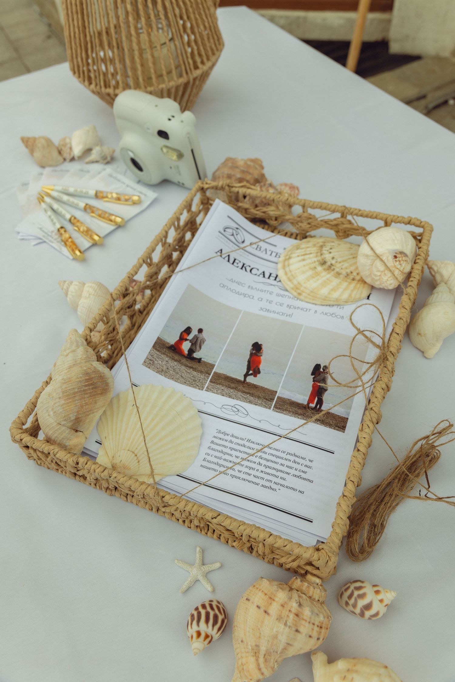 Wedding seating chart displayed in wicker tray decorated with seashells and starfish on white table.