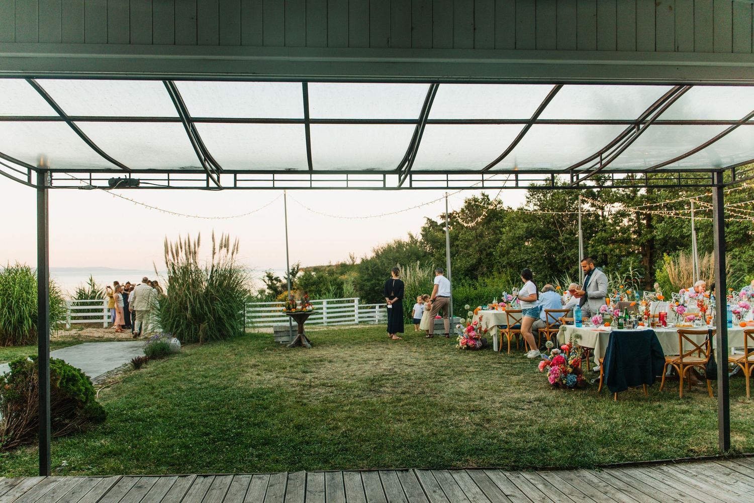 Elegant outdoor wedding reception setup on a waterfront lawn with decorated tables at dusk.
