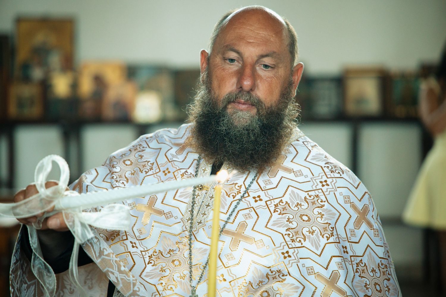 Orthodox priest with beard in ornate white and gold vestments performing a religious wedding ceremony.