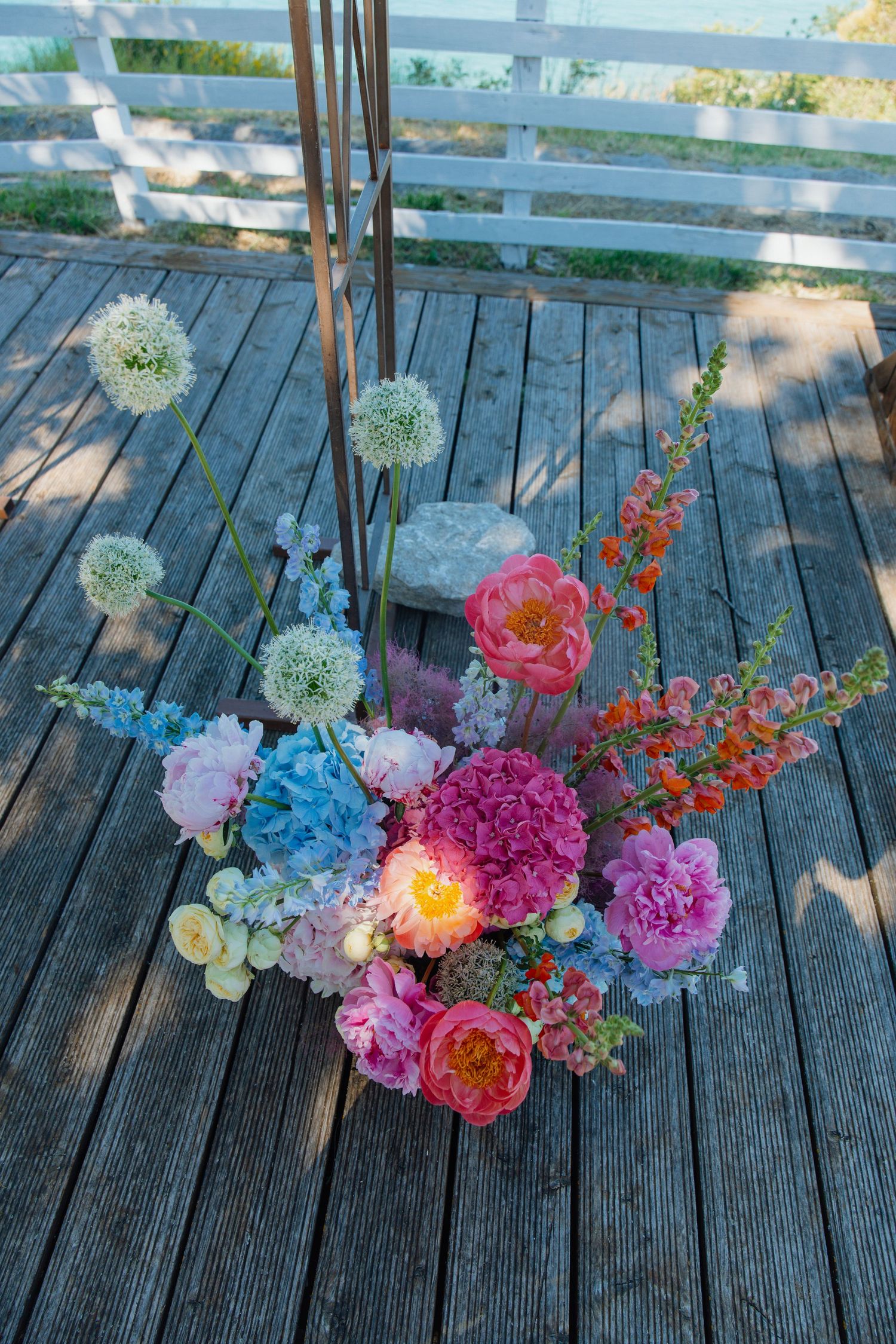 Vibrant floral arrangement with peonies, alliums, and hydrangeas on a rustic wooden deck.