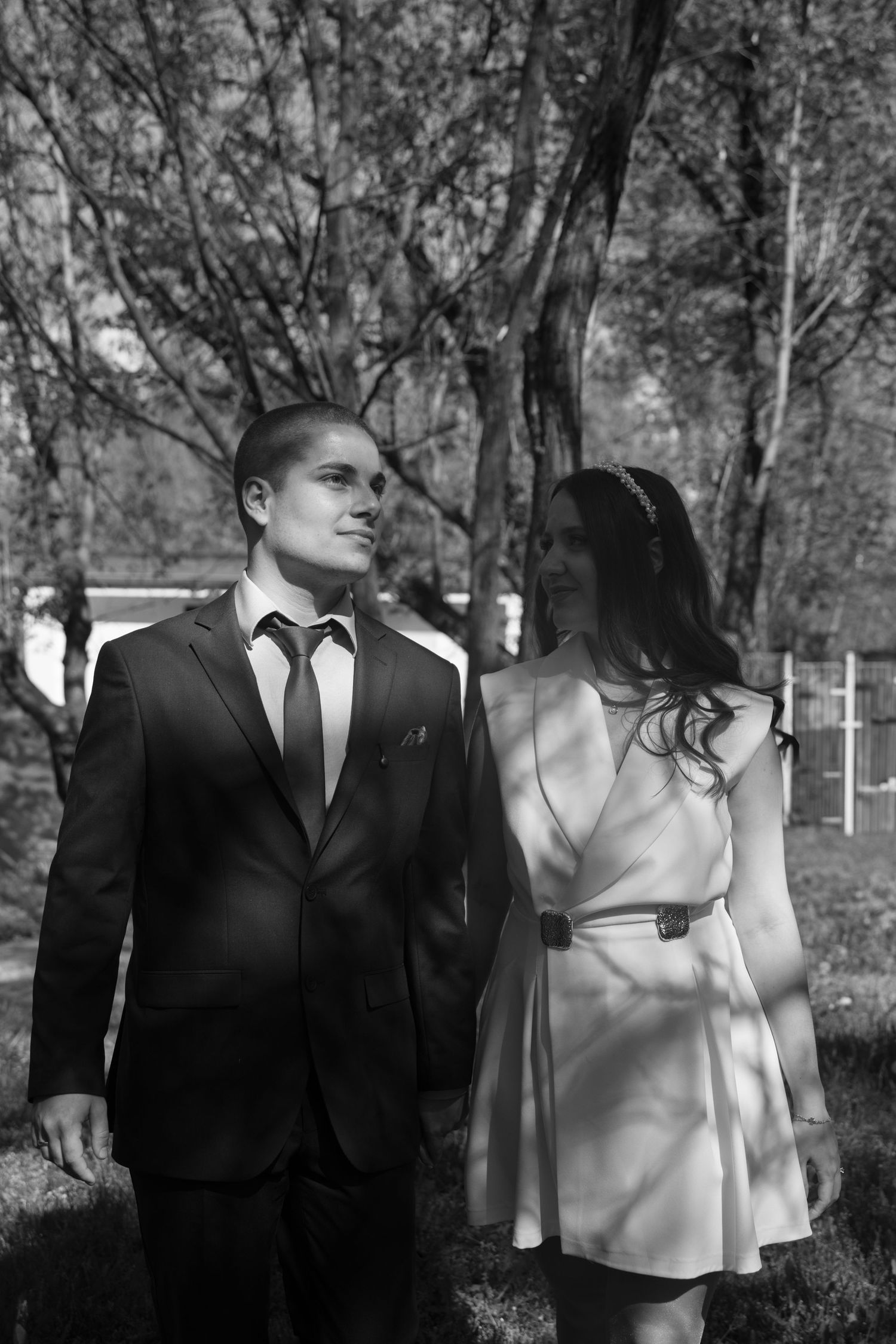 Black and white photo of bride and groom walking together in a sunlit outdoor park setting.