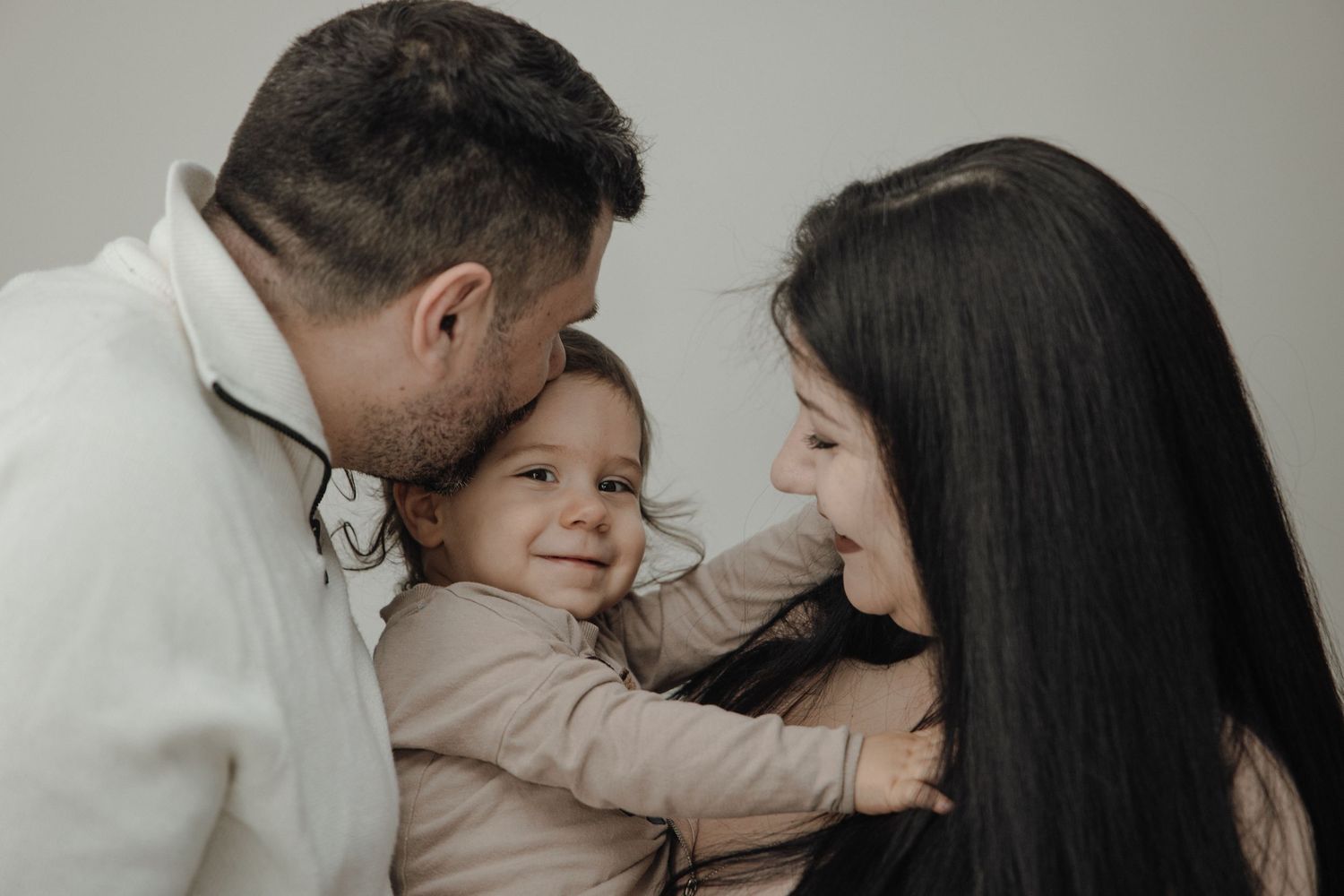 Parents lovingly kissing and cuddling their smiling baby in a warm family portrait.