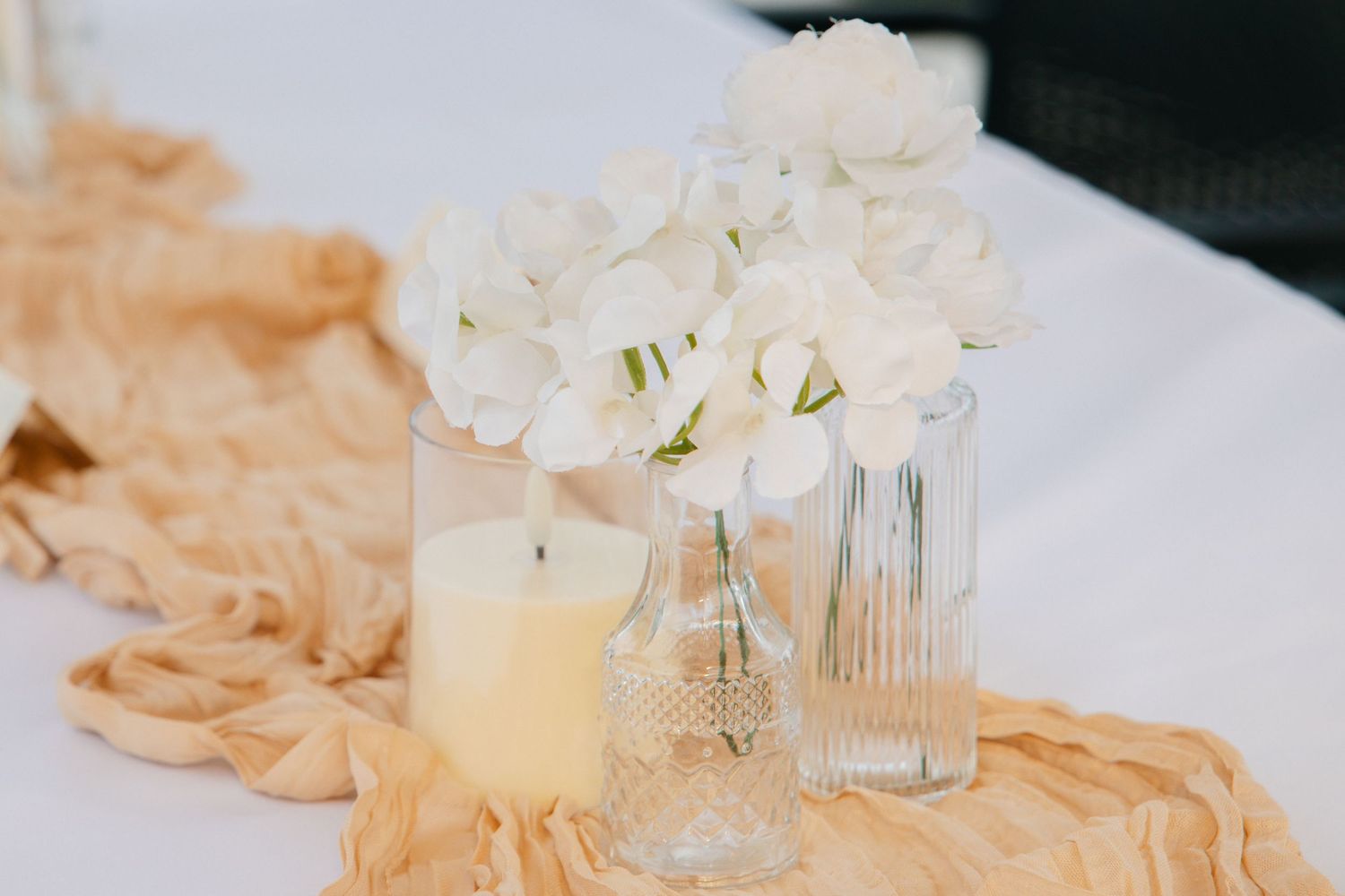 White hydrangea floral centerpiece with candle and glass vases on wedding table.