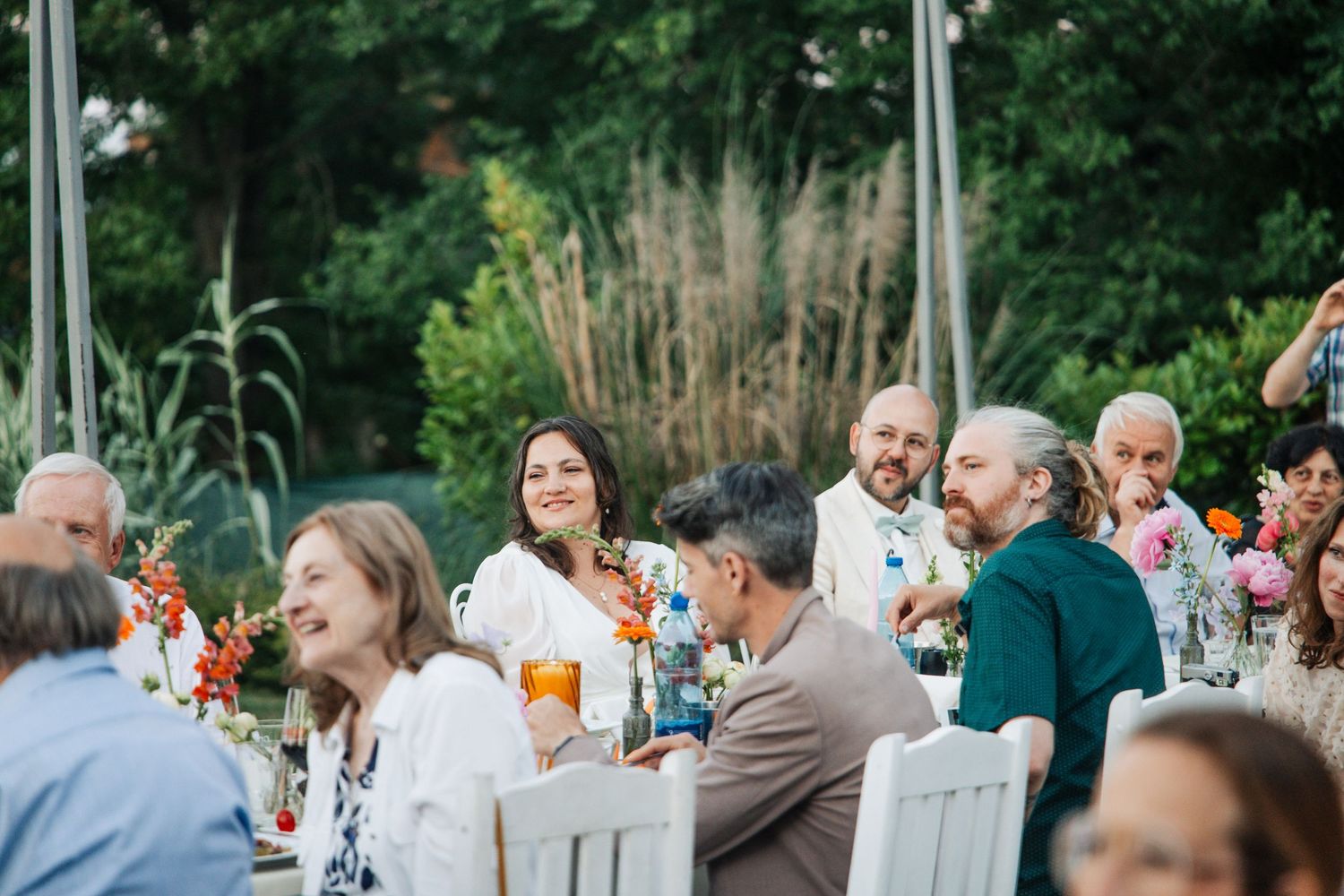Wedding guests laughing and socializing at colorful outdoor reception tables surrounded by lush greenery.