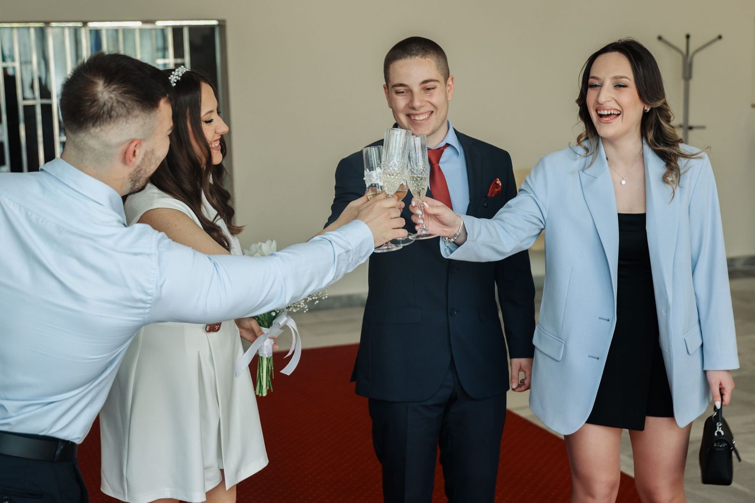 Four elegantly dressed people toasting with champagne glasses at a celebratory event or wedding reception.