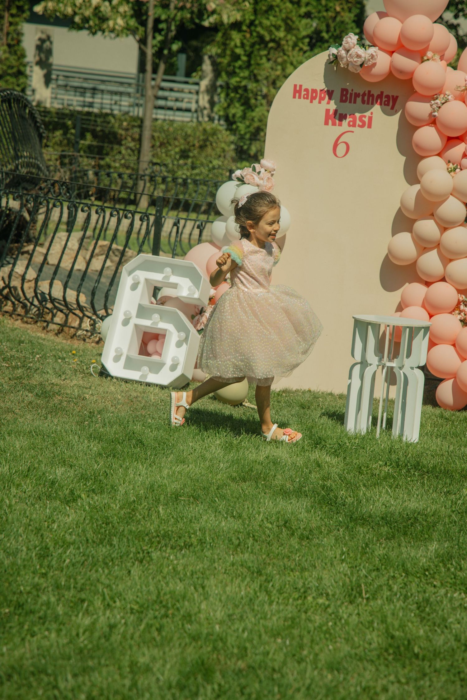 A young girl in a pink tutu dress celebrates her 6th birthday outdoors with balloon decorations.