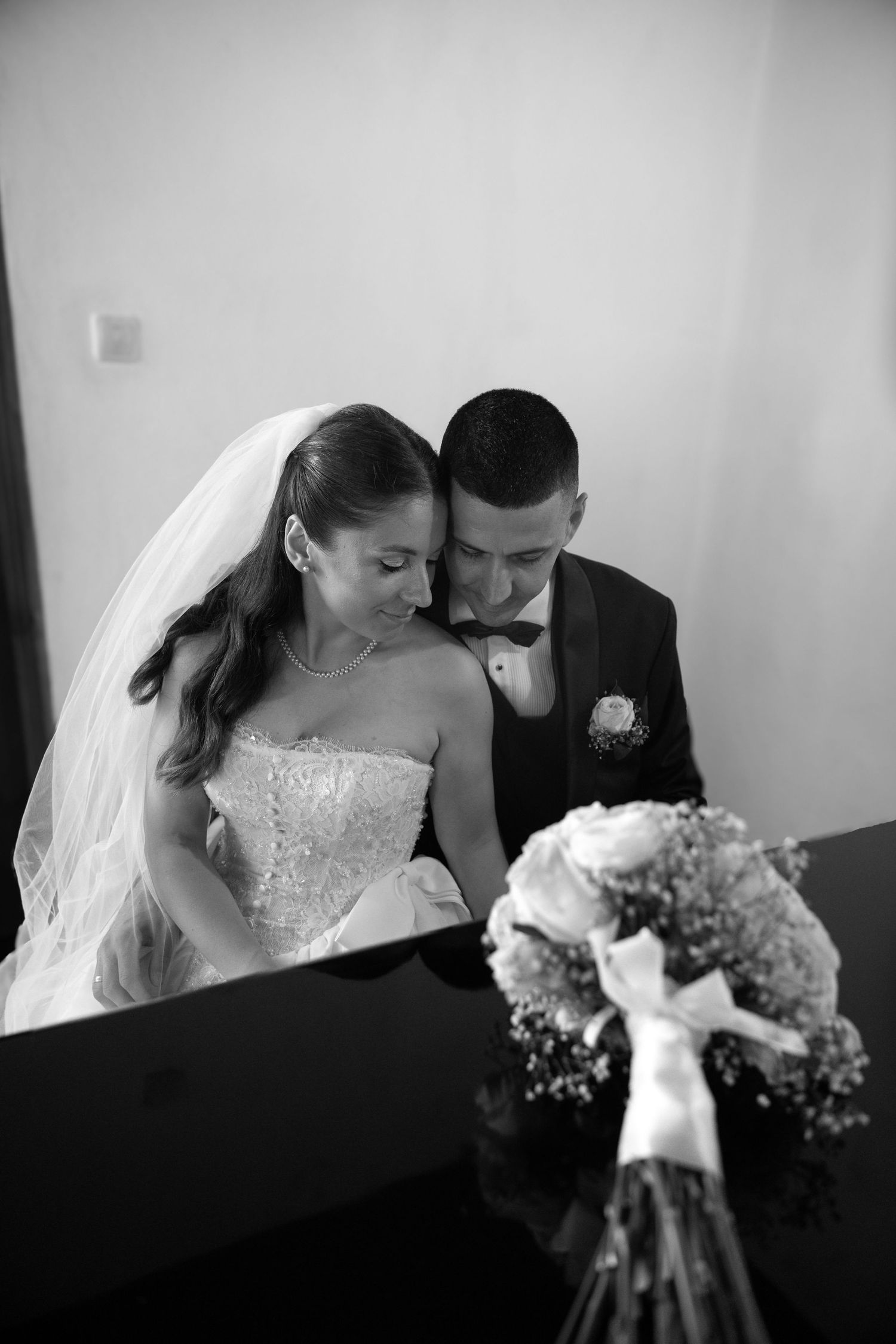 Black and white photo of a bride and groom sharing an intimate moment, with a bridal bouquet in the foreground.