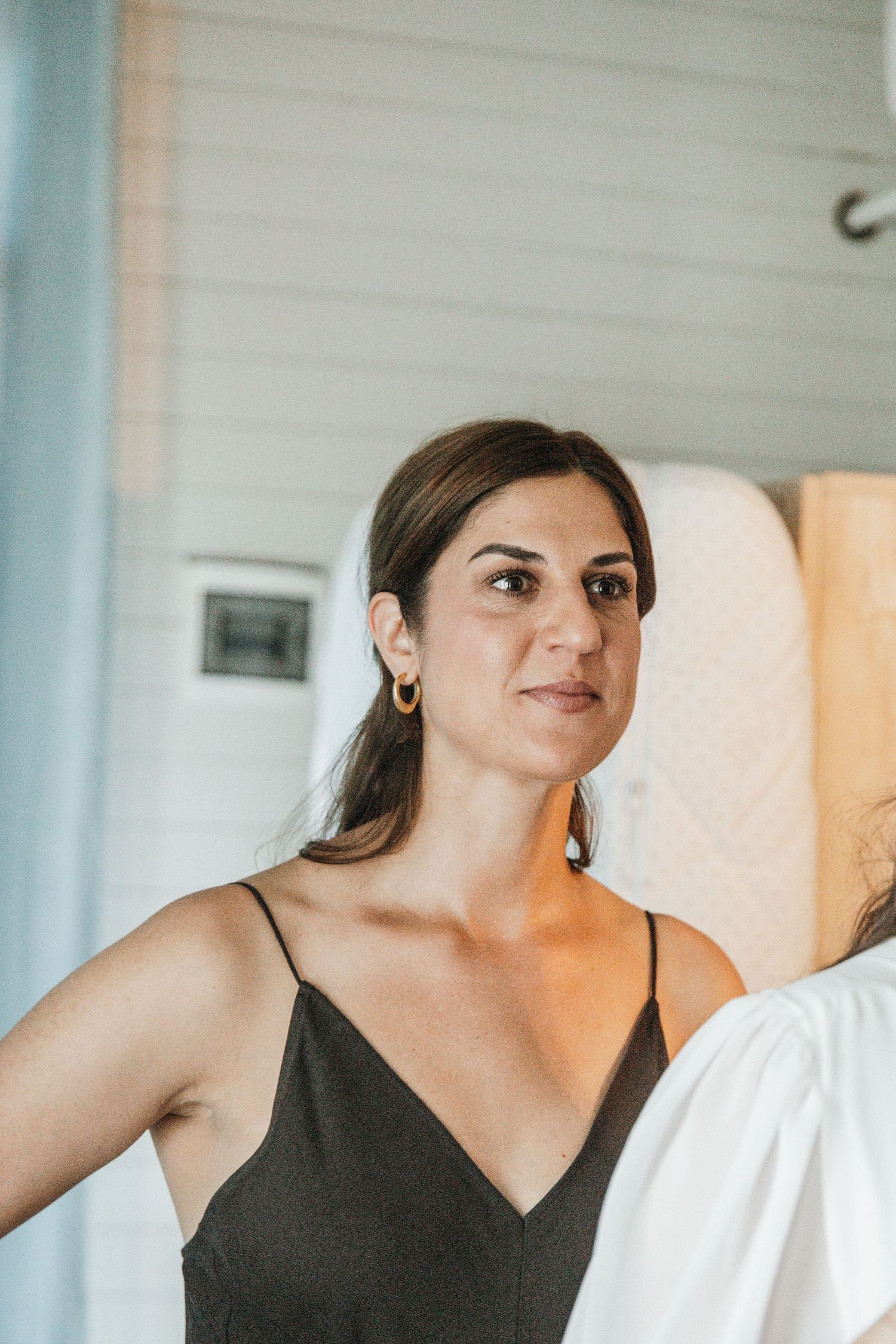 Brunette woman in black satin dress with gold hoop earrings at wedding preparation.