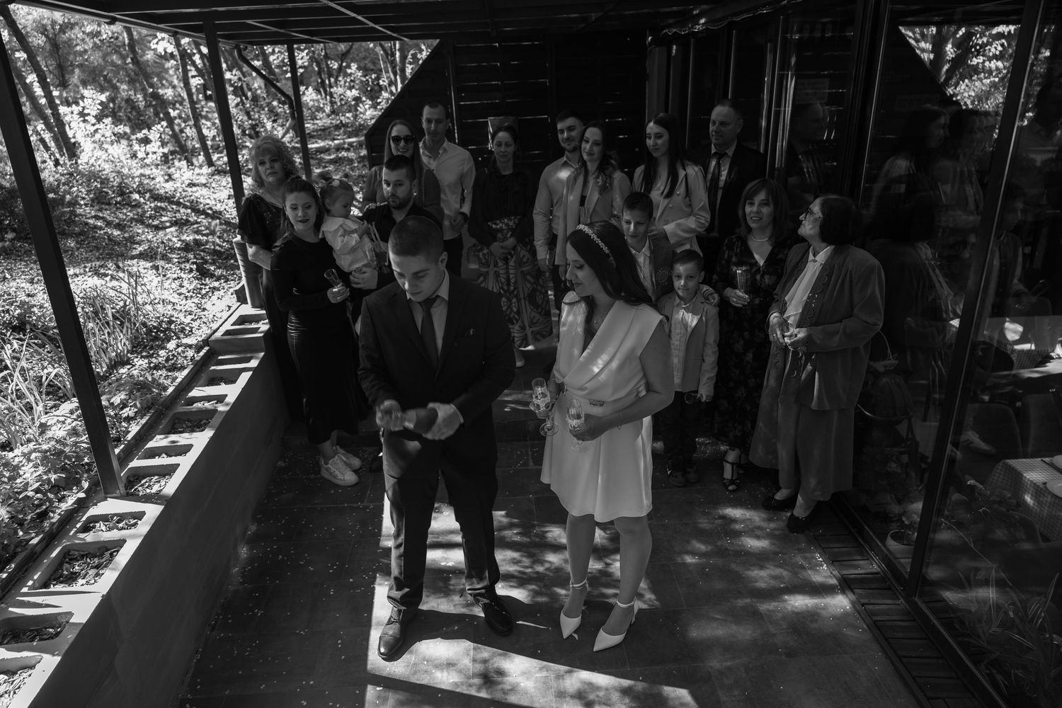 Black and white photo of a wedding couple exchanging vows on a covered outdoor venue with guests gathered behind them.