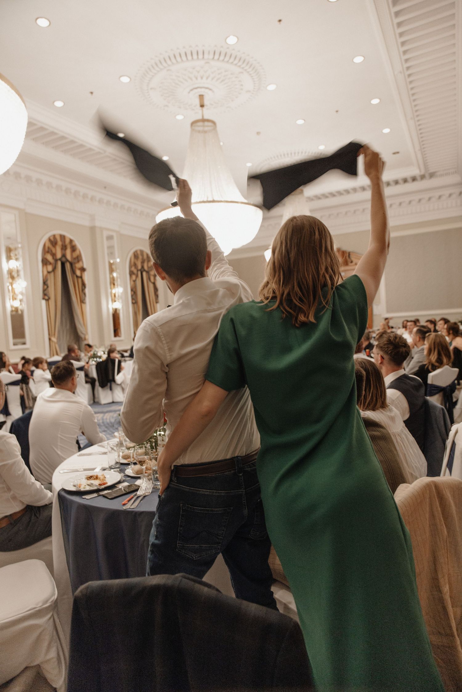 Guests celebrating at a wedding reception in an elegant ballroom, waving napkins in the air.