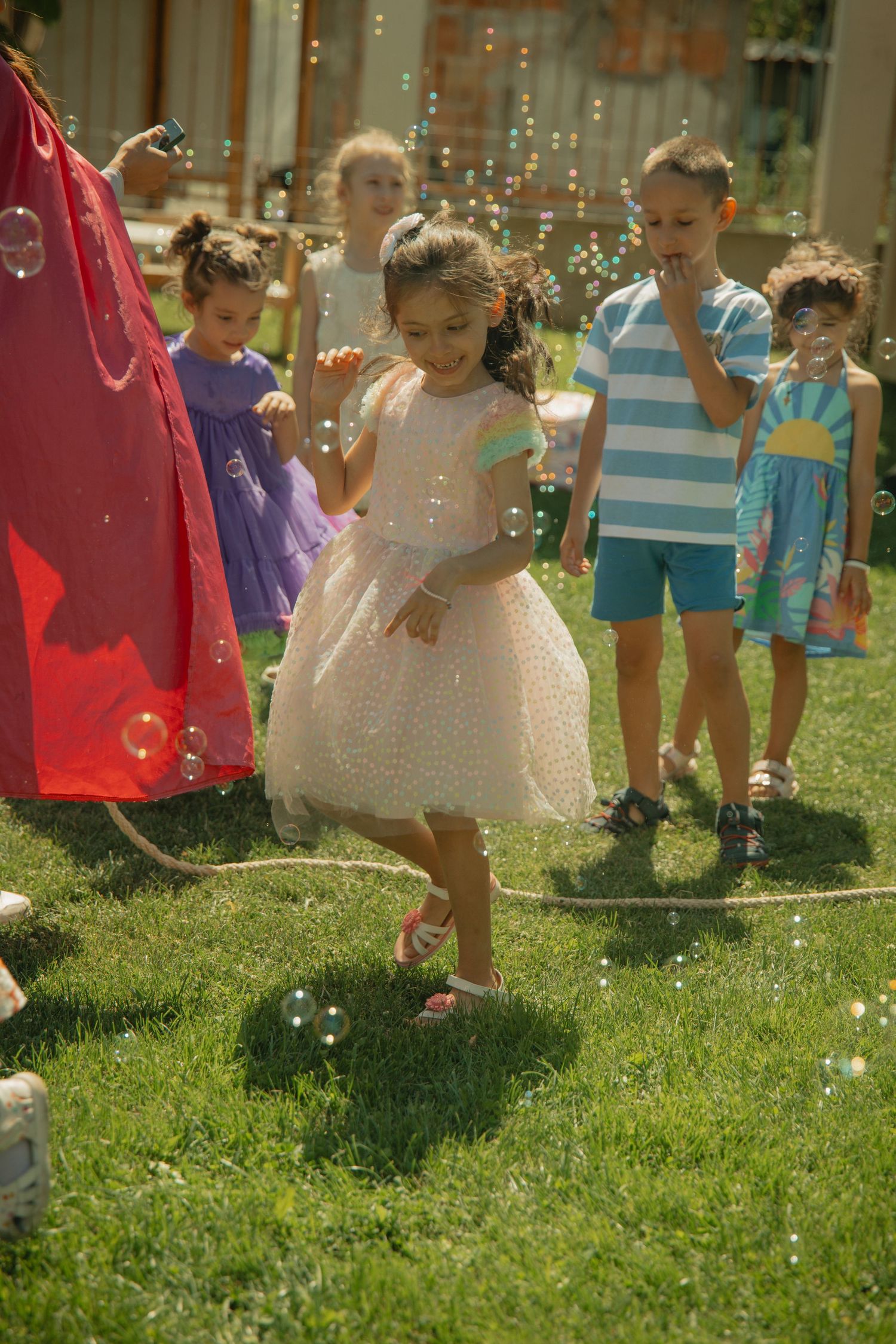 Children playing with soap bubbles at an outdoor birthday party on green grass.