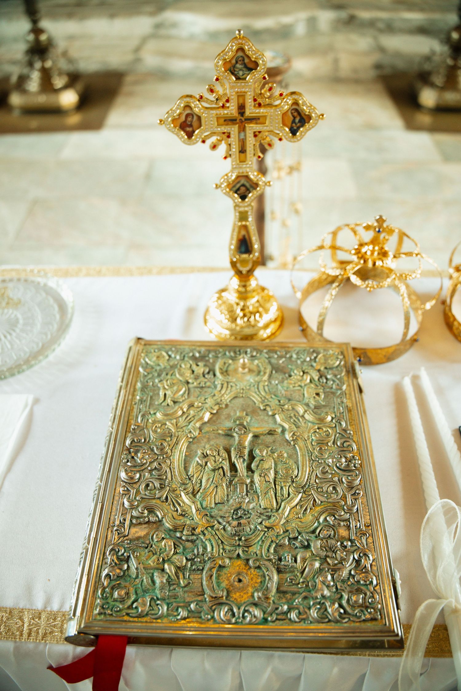 Orthodox wedding ceremony items including ornate gold cross, crown, and decorative religious Bible on white altar.
