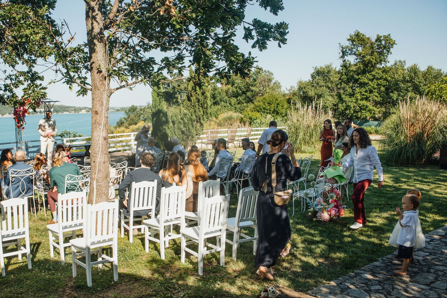 Guests gathering on lawn with white chairs for outdoor waterfront wedding ceremony.