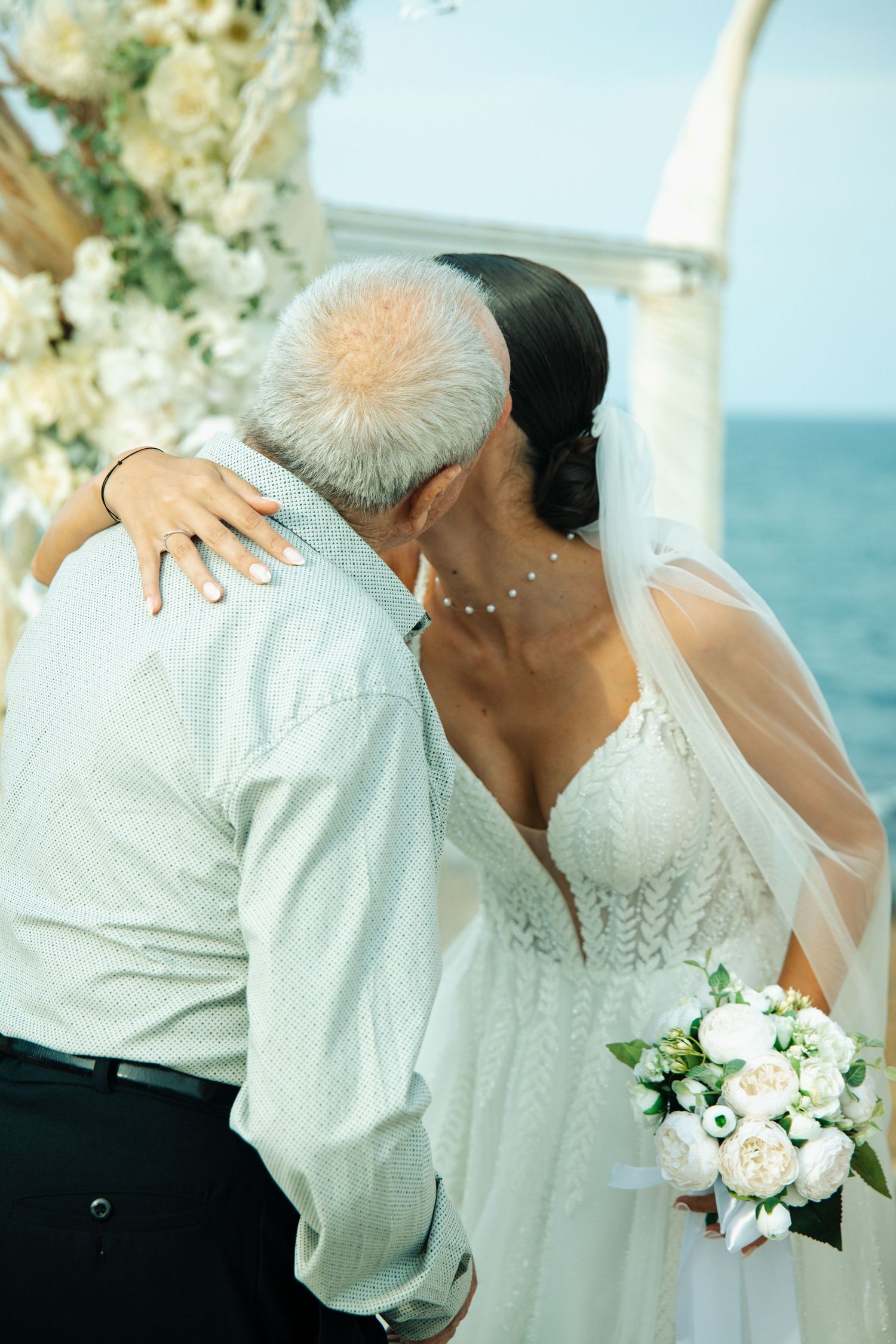 Bride and groom share a romantic kiss at an outdoor seaside wedding ceremony with white floral arch.