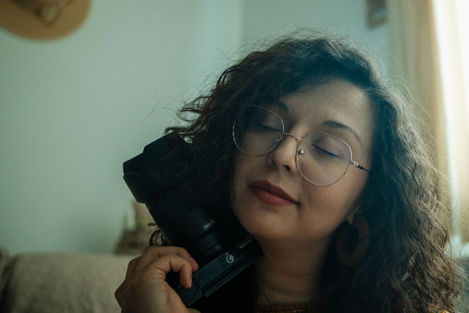 Woman with curly dark hair and glasses poses in a series of artistic self portraits against a light background.