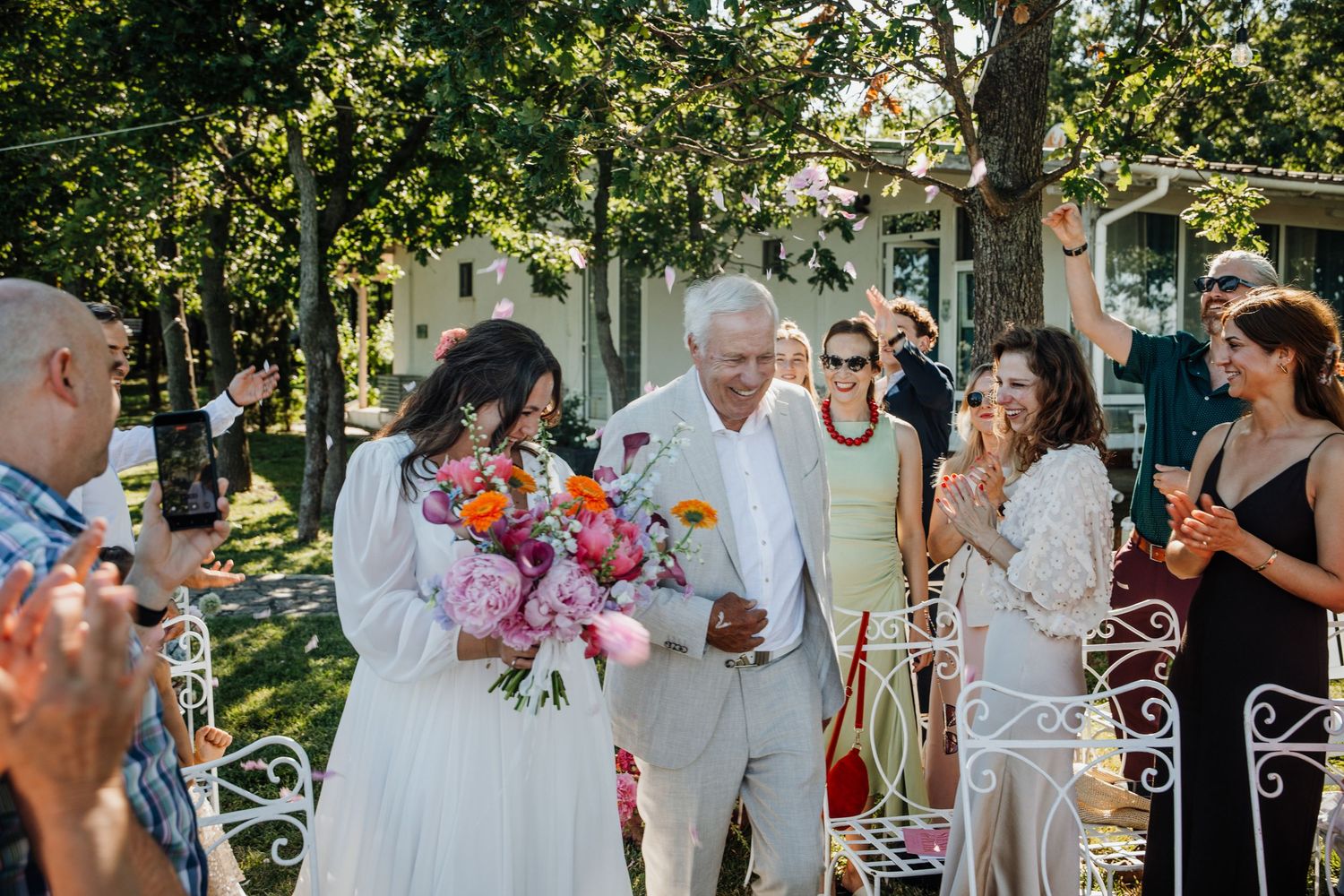 Bride and groom walk through cheering guests at outdoor garden wedding ceremony.