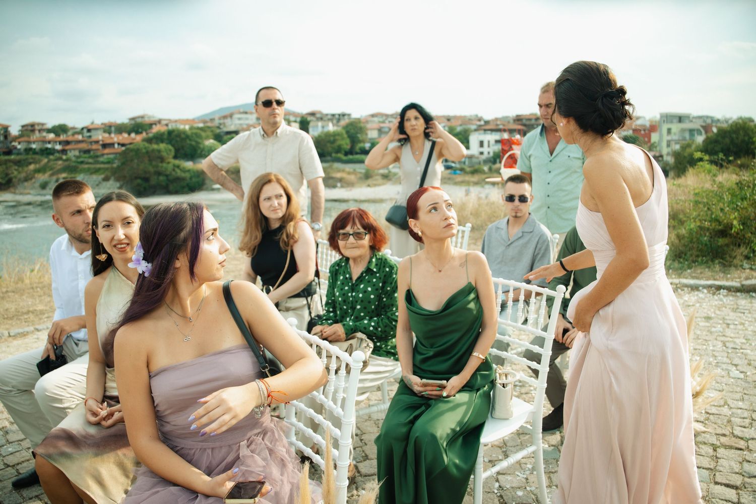 Group of wedding guests socializing outdoors by the seaside, women in elegant dresses enjoying a ceremony gathering.