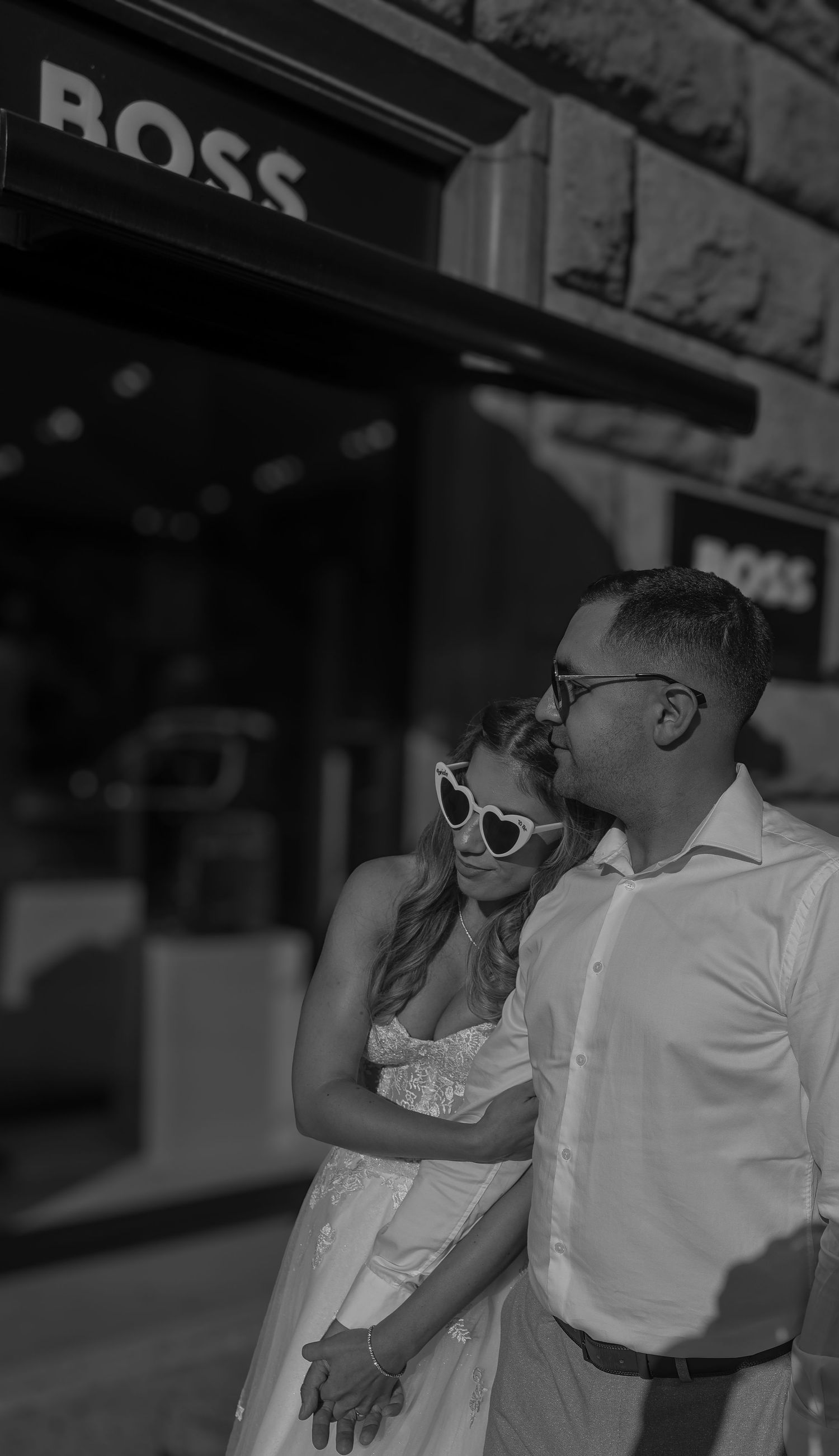 Black and white photo of a couple in wedding attire embracing outside a Hugo Boss store.