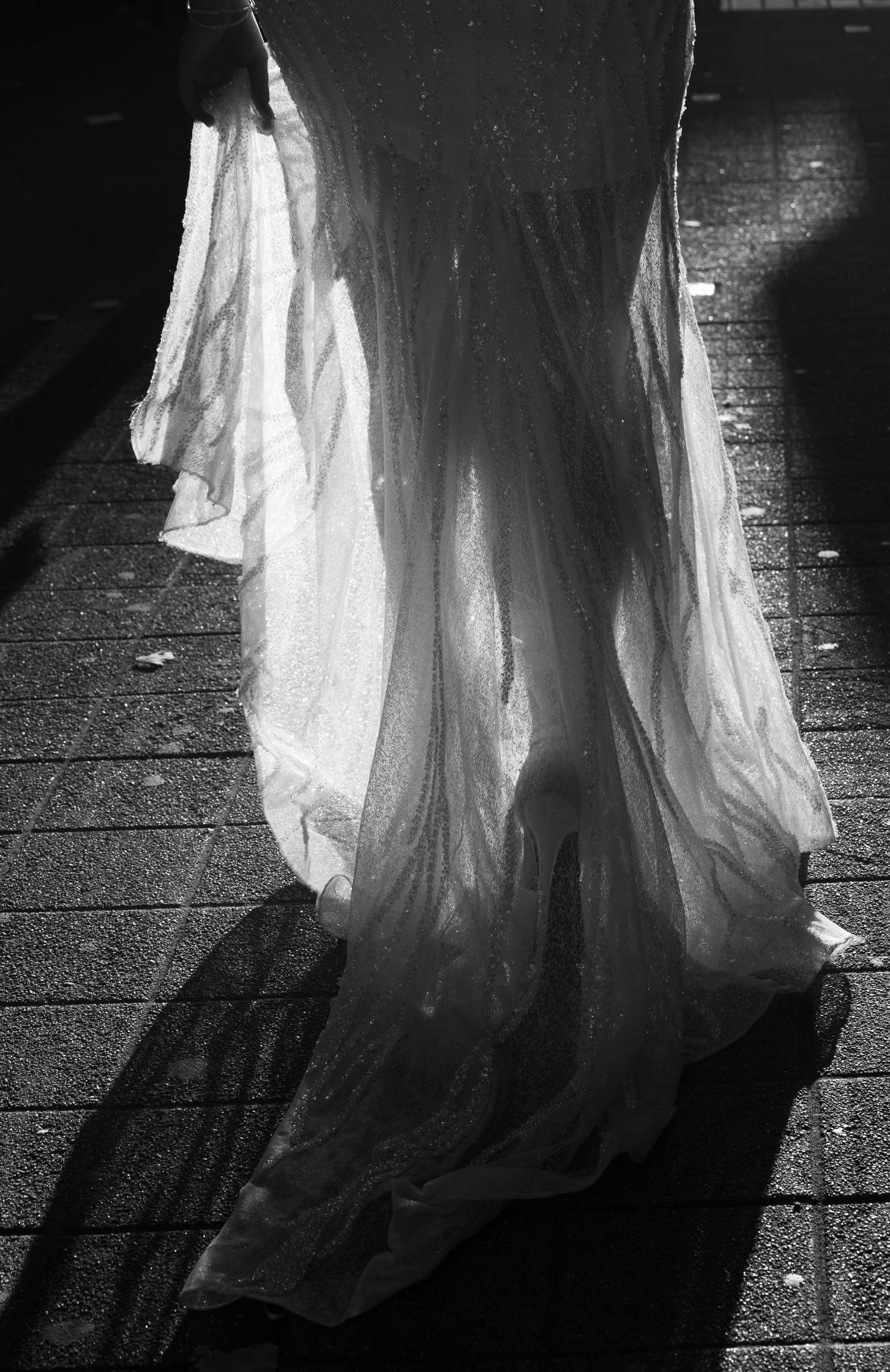Black and white photo of a flowing white fabric dress casting dramatic shadows on a wet cobblestone pavement.