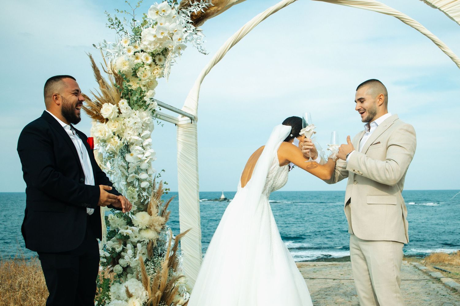 Couple exchanging vows at outdoor beach wedding ceremony with floral arch and ocean backdrop.