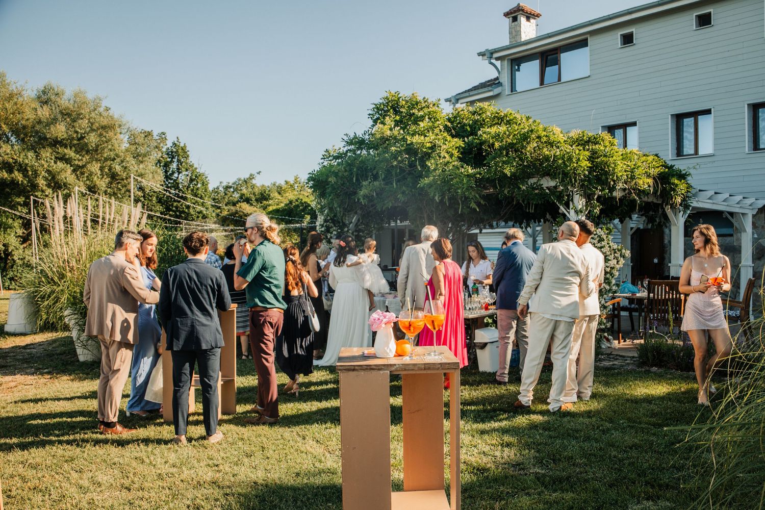 Wedding guests mingling on lawn outside rustic venue during outdoor cocktail hour.