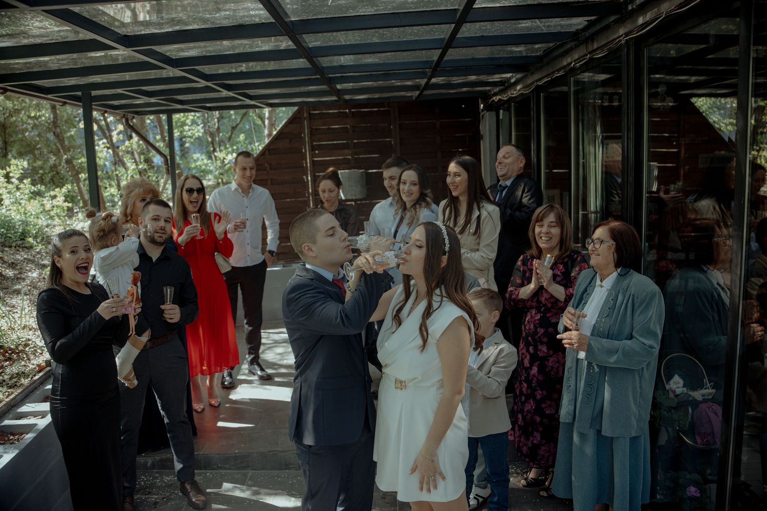 Couple sharing a toast with guests at an intimate outdoor wedding reception near a rustic wooden cabin.