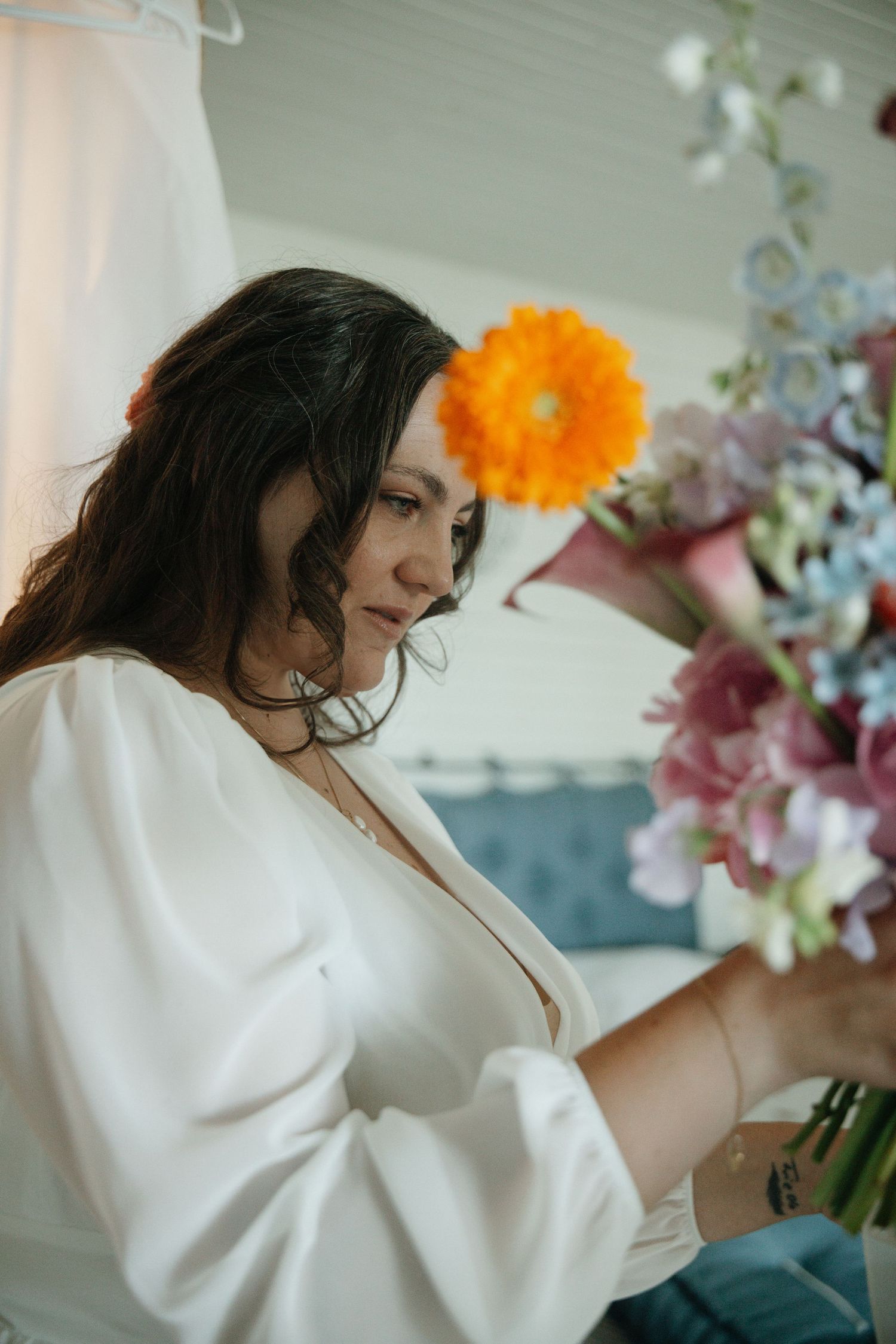 Woman in white dress smelling a colorful bouquet with orange gerbera daisy at a wedding.