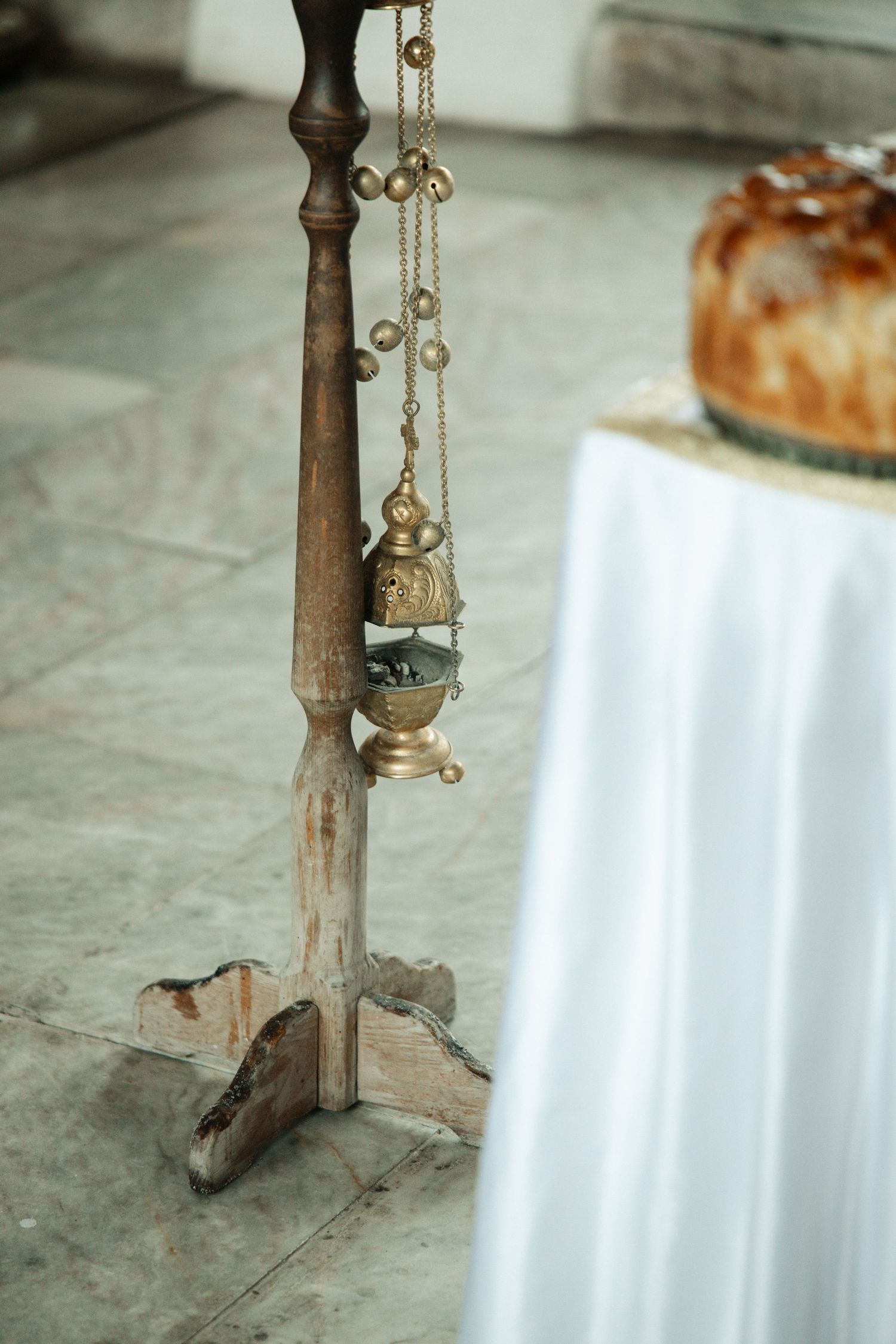 Ornate golden censer hanging from wooden stand on stone floor at church.