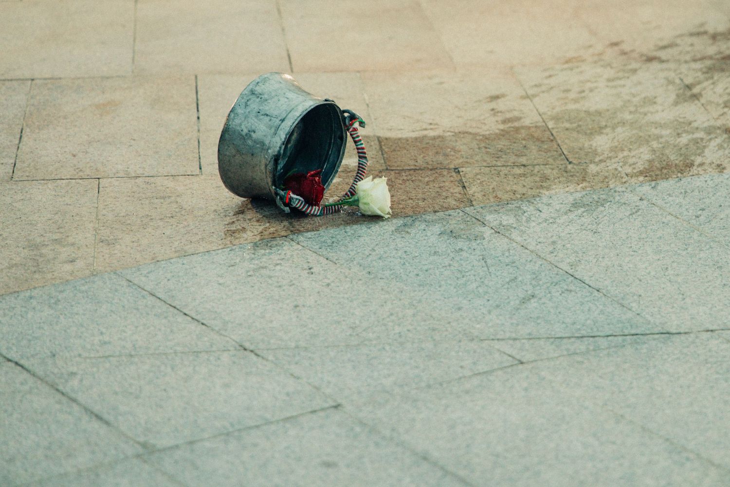 Overturned metal bucket with scattered items on stone pavement outdoors.