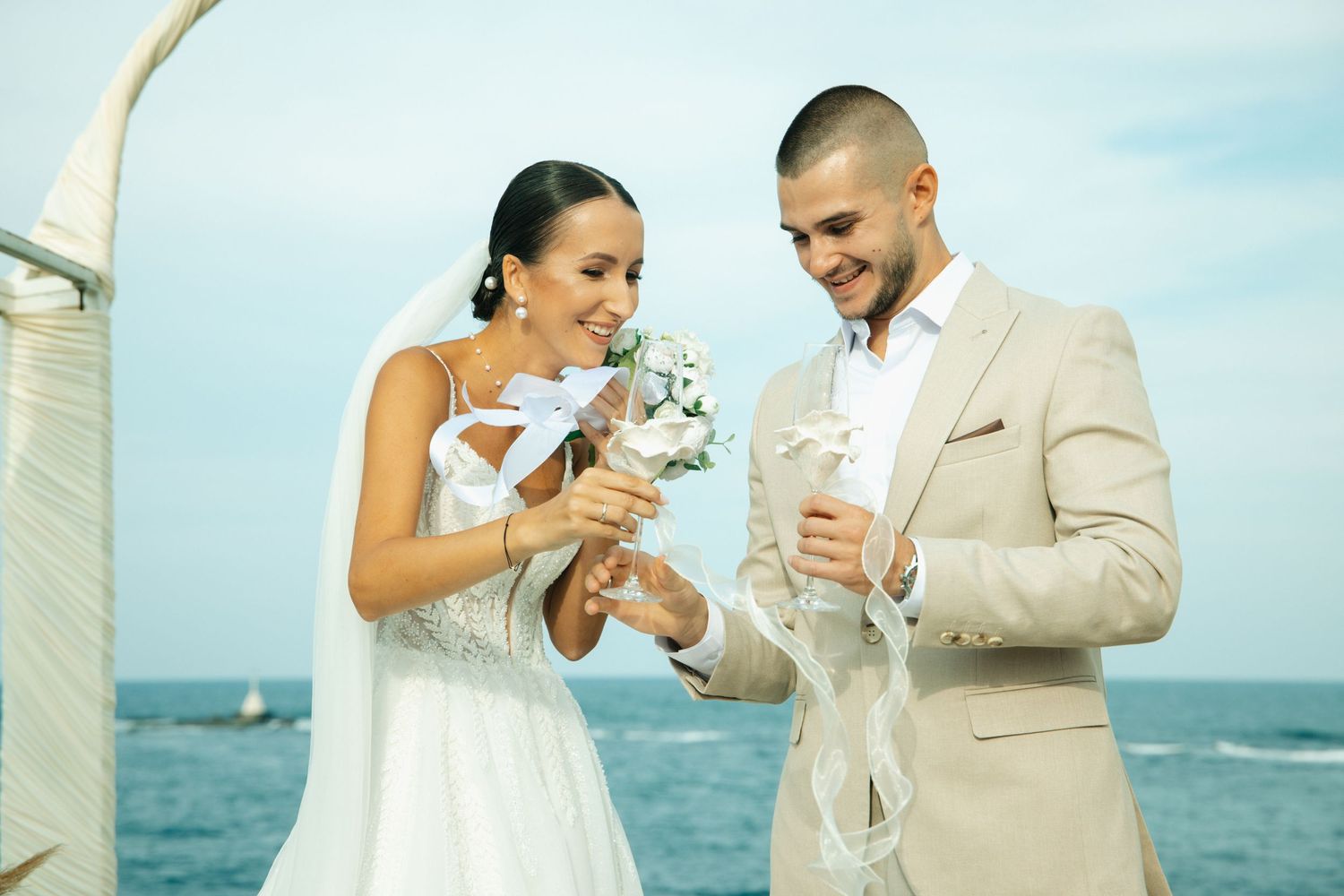 Bride and groom smiling during outdoor beach wedding ceremony, exchanging rings with ocean backdrop.