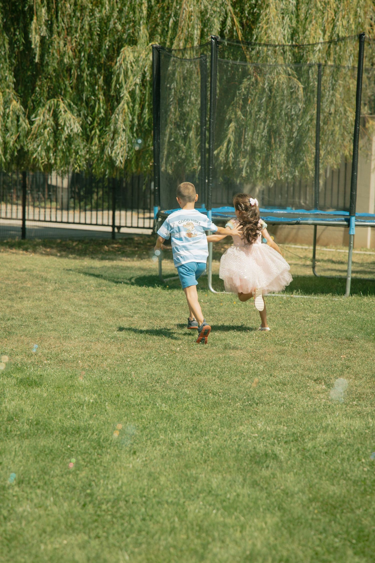 Two children holding hands running across green grass at outdoor birthday party.