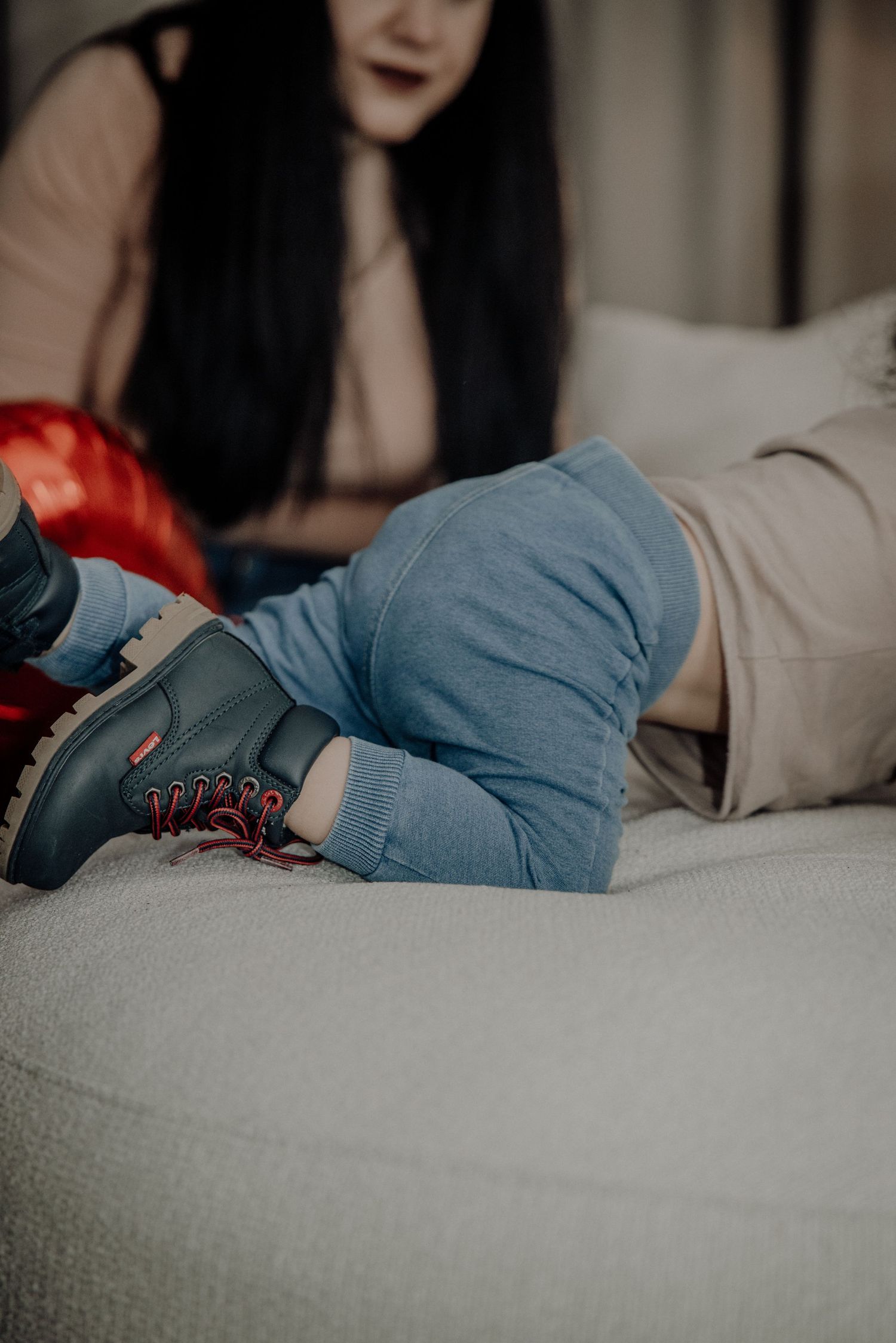 Woman in blue jeans and dark boots with red laces relaxing on a white sofa.