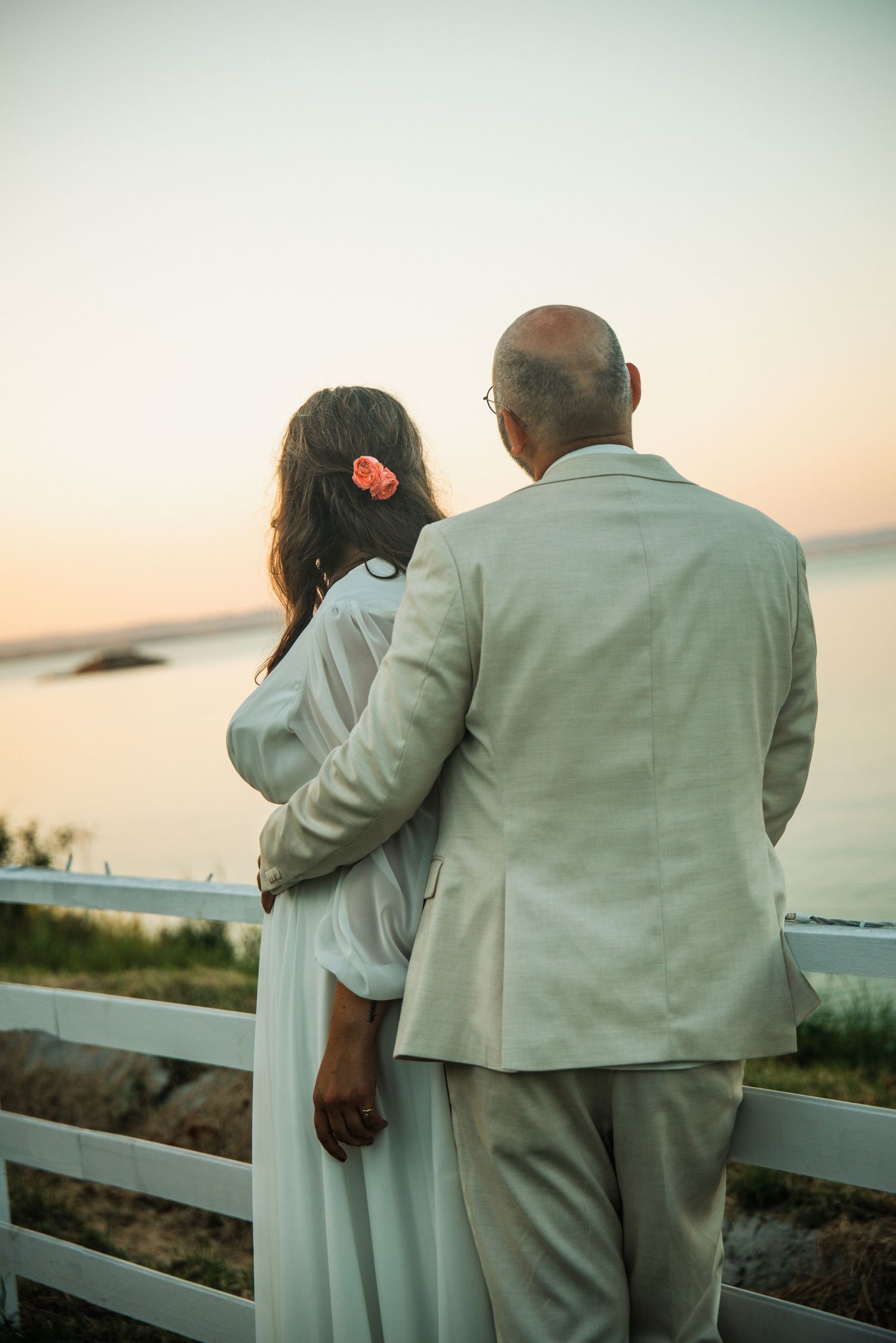 Bride and groom embracing while watching a romantic sunset over the ocean at their wedding.