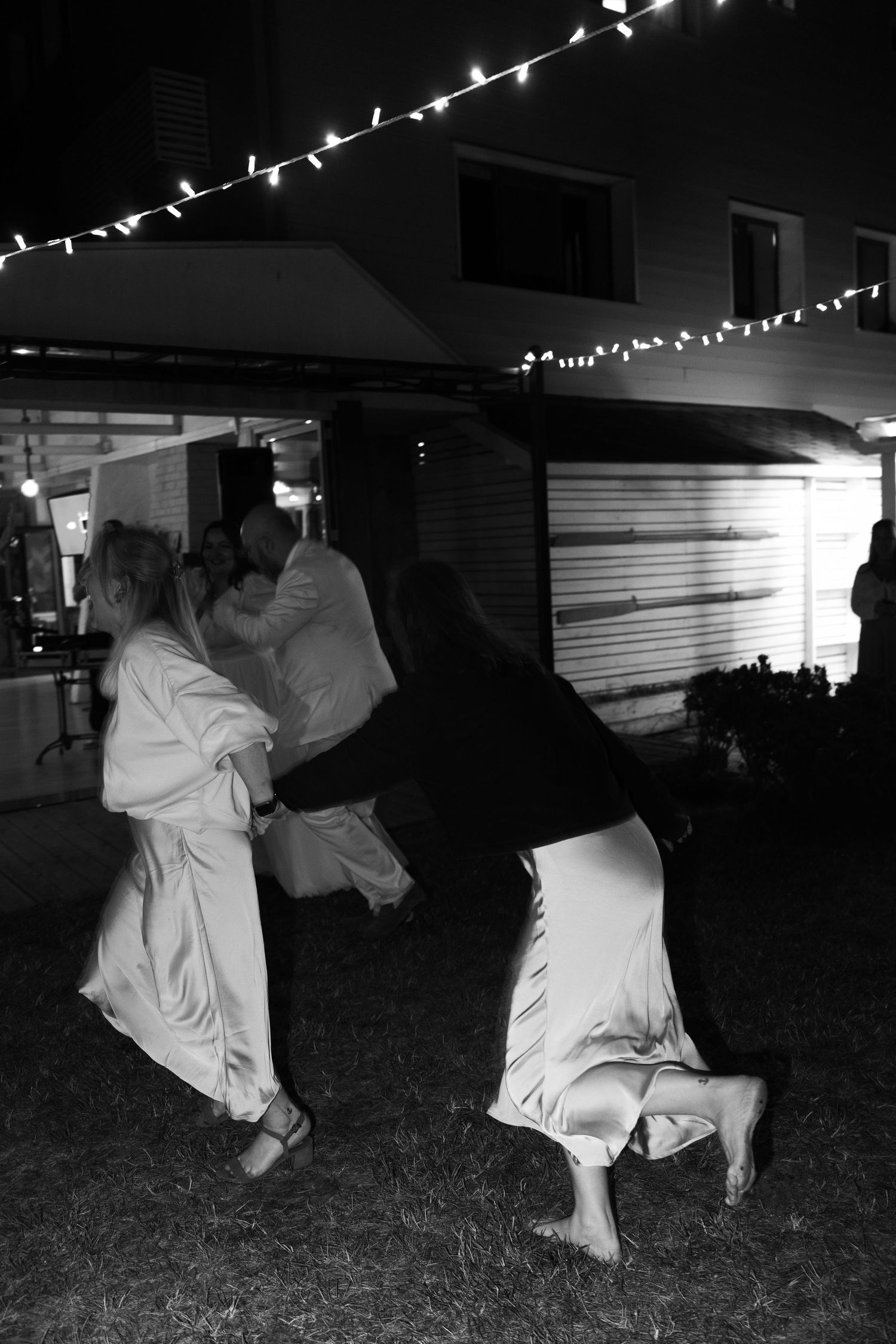 Black and white photo of guests dancing energetically at an outdoor nighttime wedding reception.