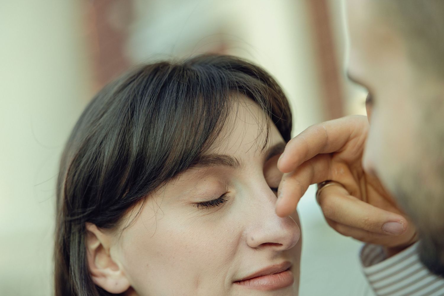 A woman with closed eyes receives a professional makeup application with a cosmetic brush.