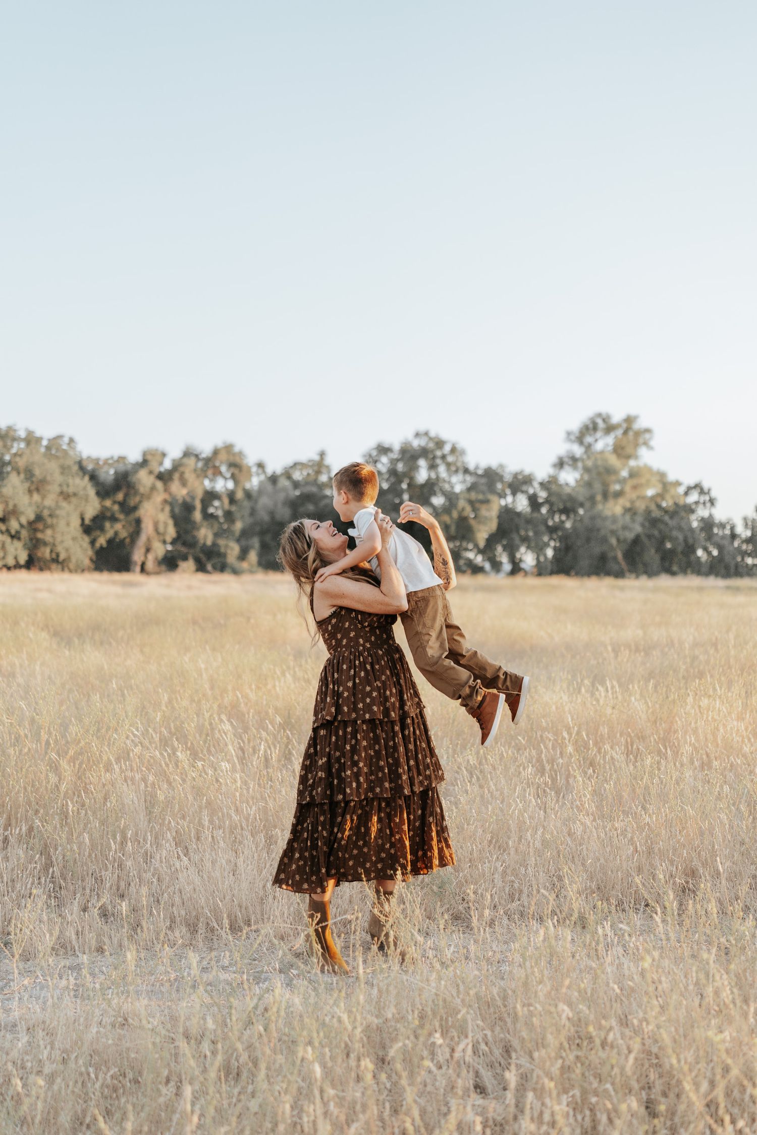 Two people wearing floral dresses dance together in a sunlit golden field on a summer afternoon.