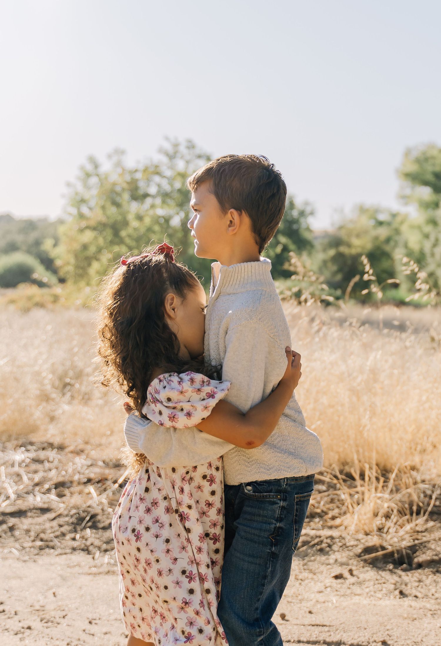 Two children share a tender embrace in a sunlit field of golden grass on a warm afternoon.