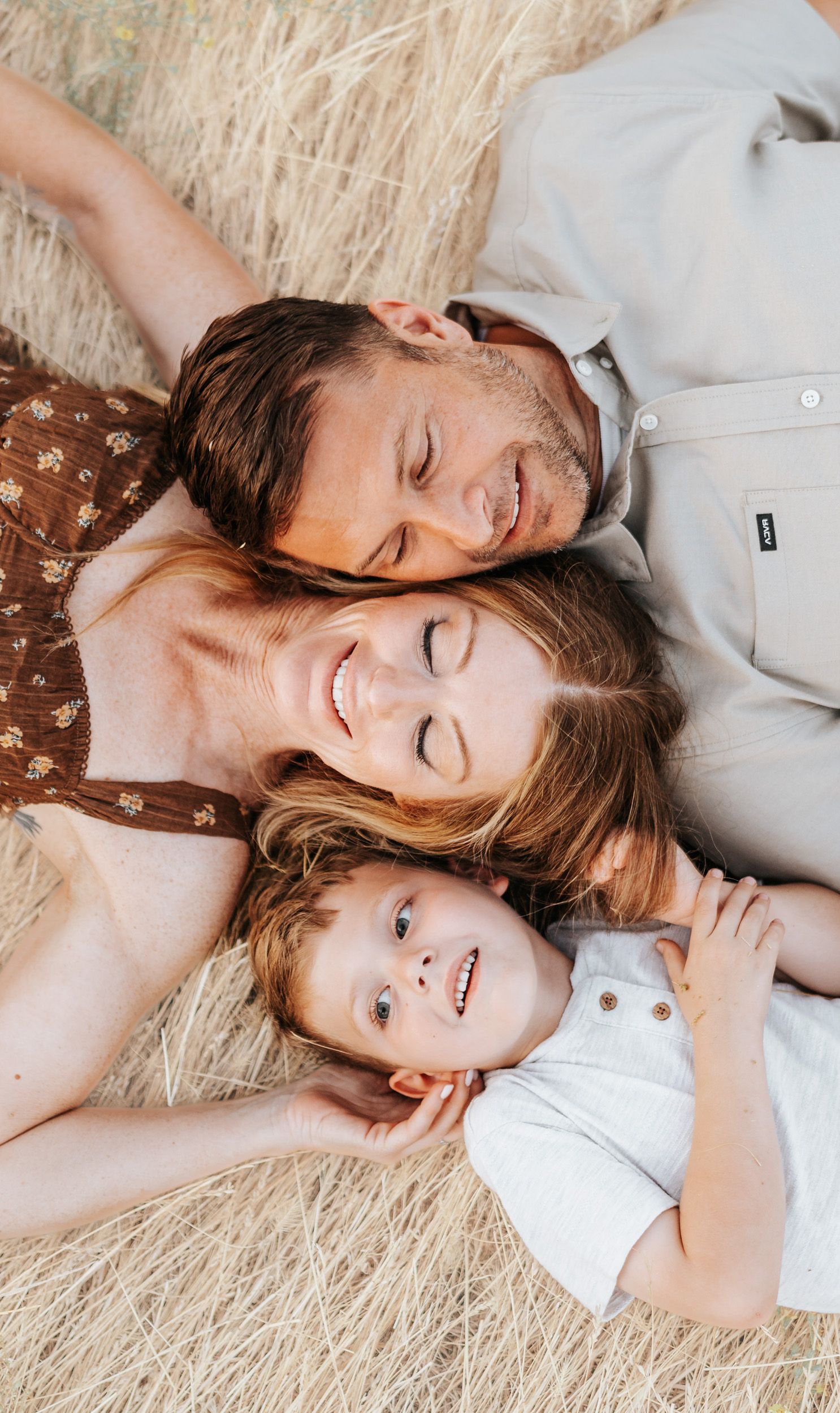 A loving family lying close together in dried grass field with peaceful expressions.