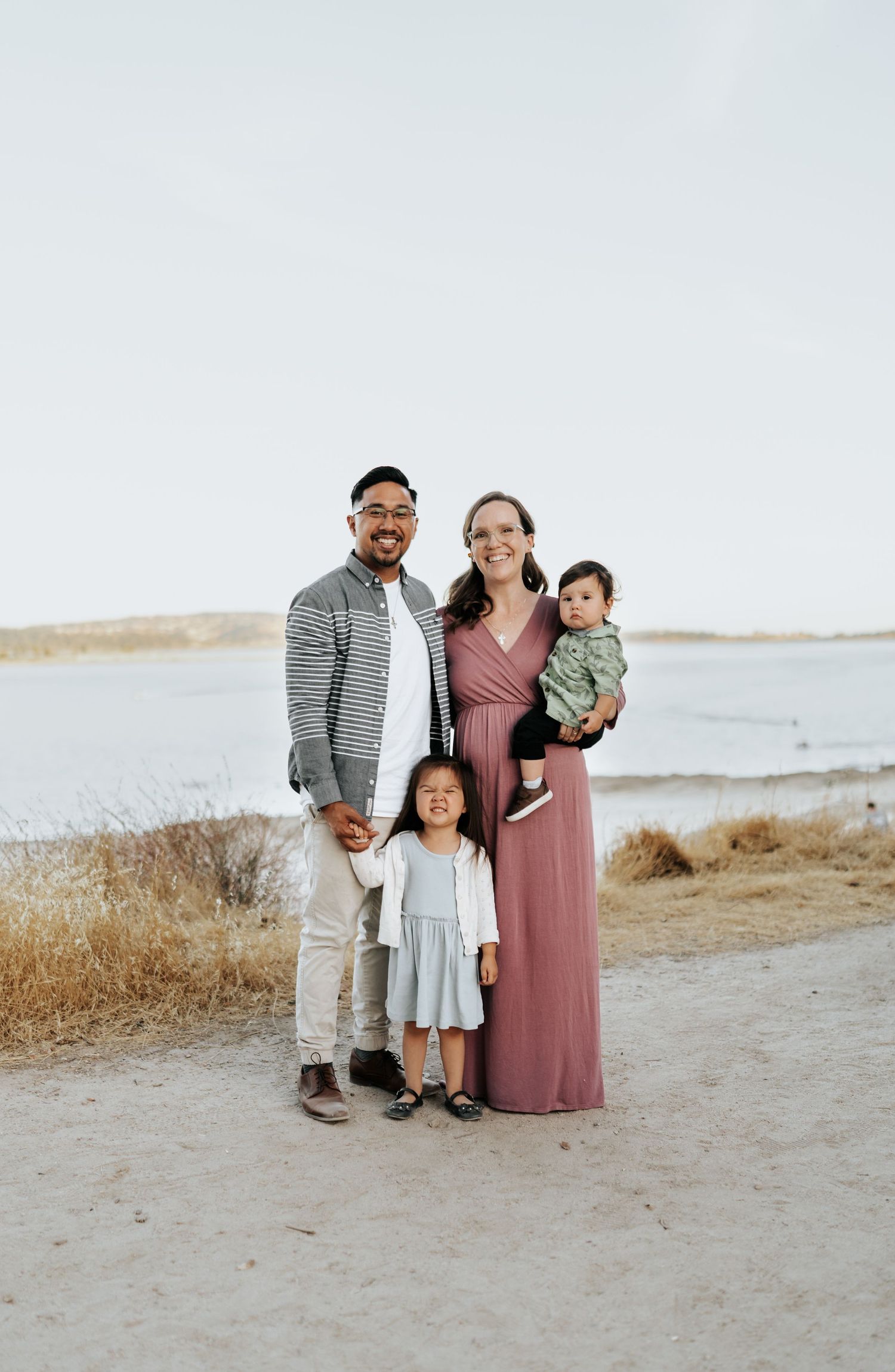 Family of four poses together on a coastal path at sunset.