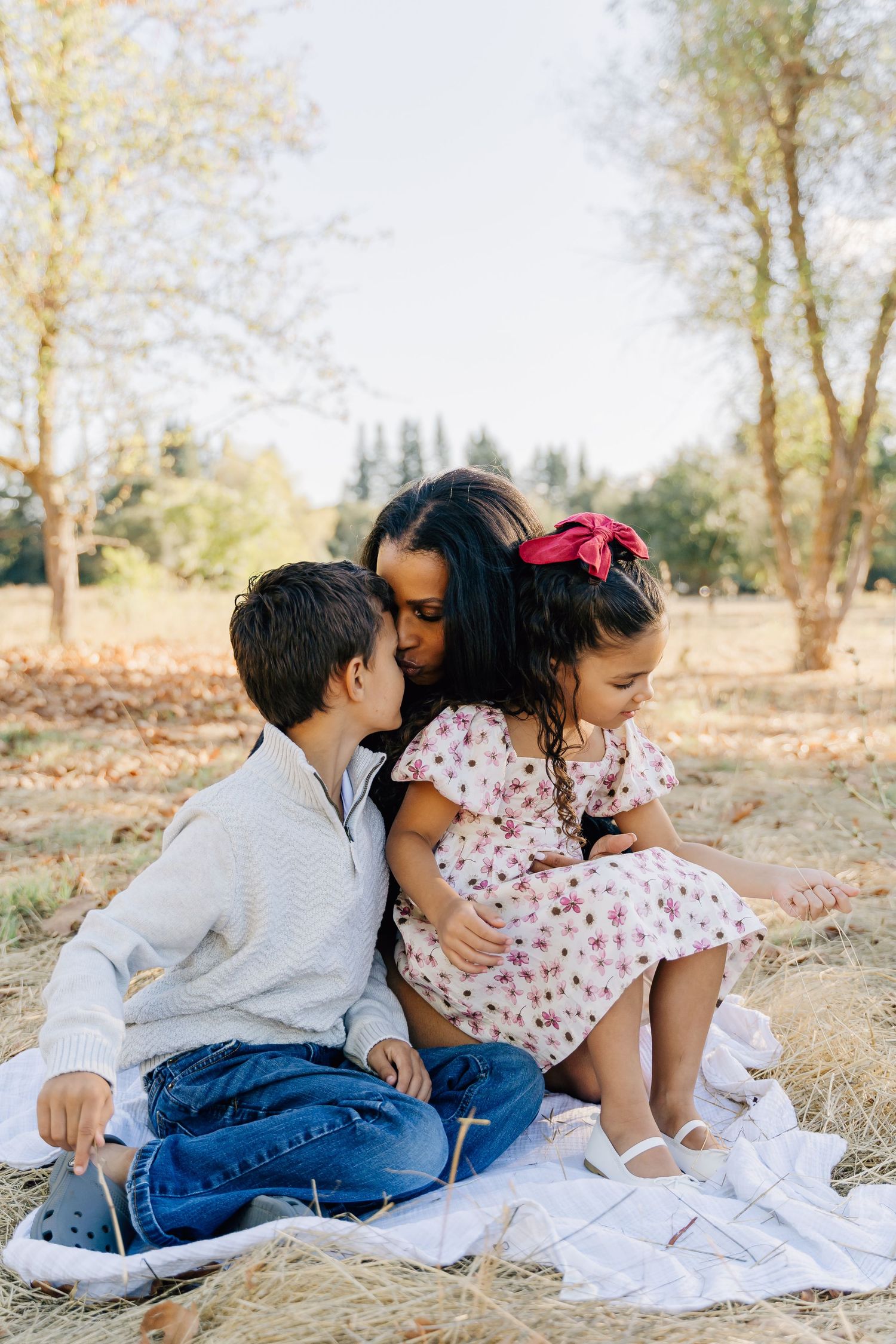A candid family photo series showing playful interactions while sitting on a white blanket outdoors.