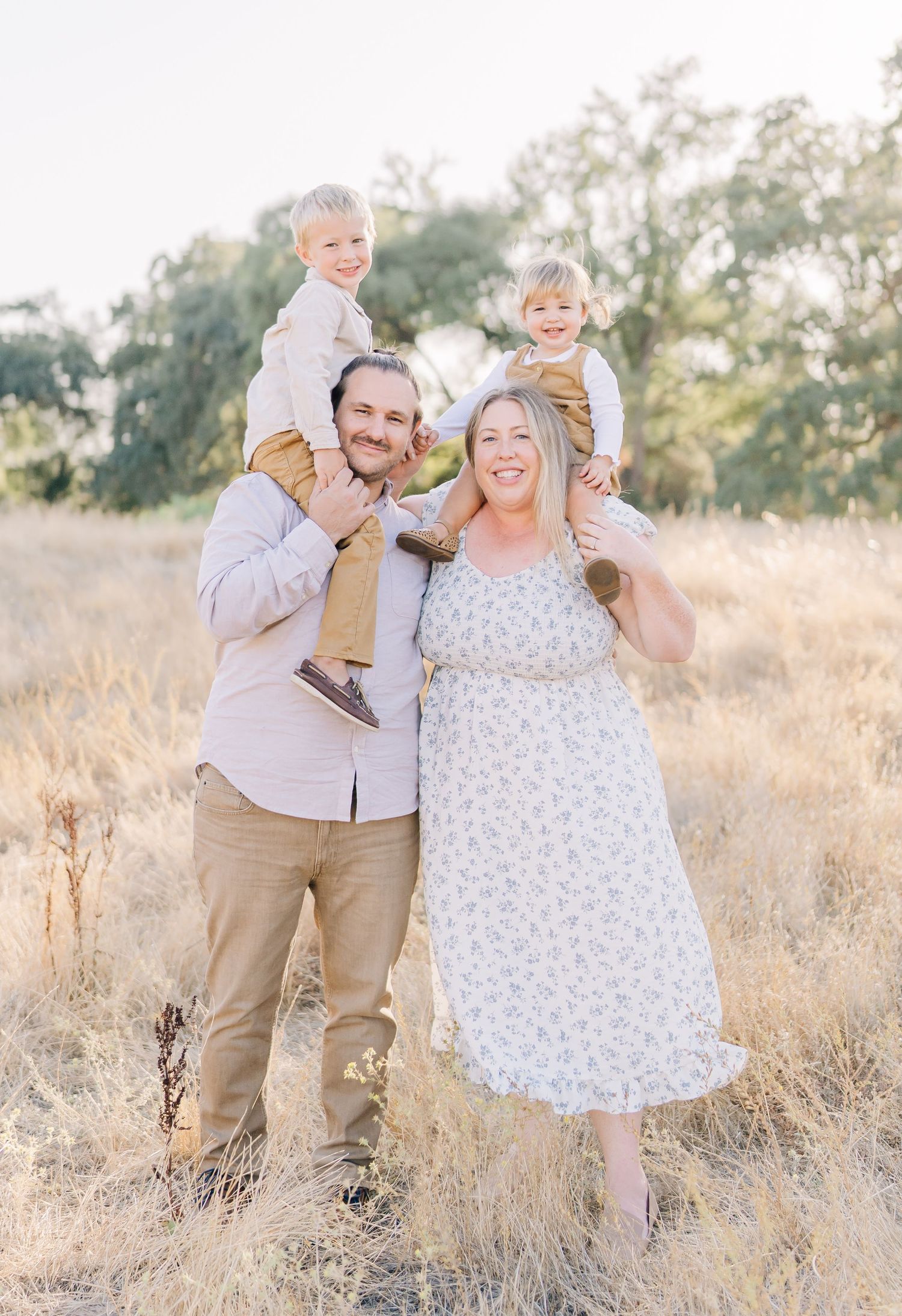A joyful family poses together in a golden field during sunset, with children sitting on shoulders.