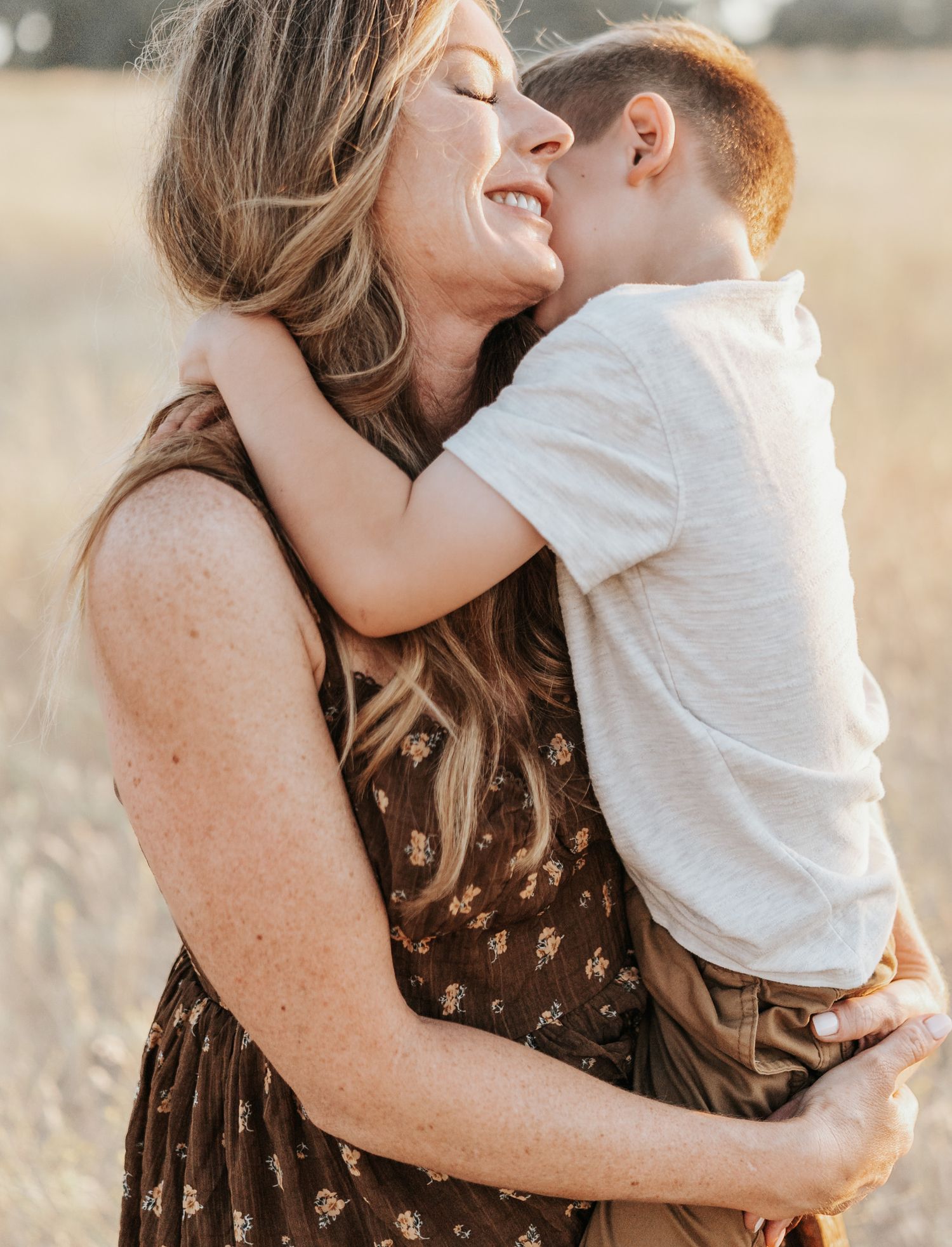 A tender moment between parent and child laughing together in golden sunlight wearing brown and white clothing.