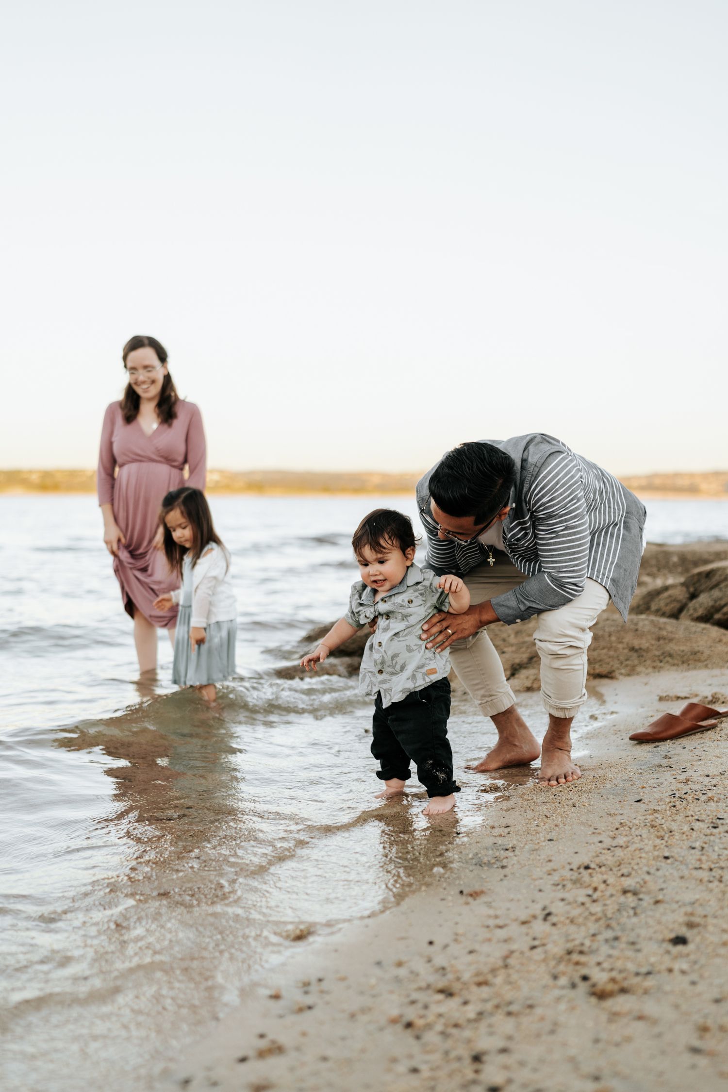 Family playing and splashing in shallow water at the beach during sunset.