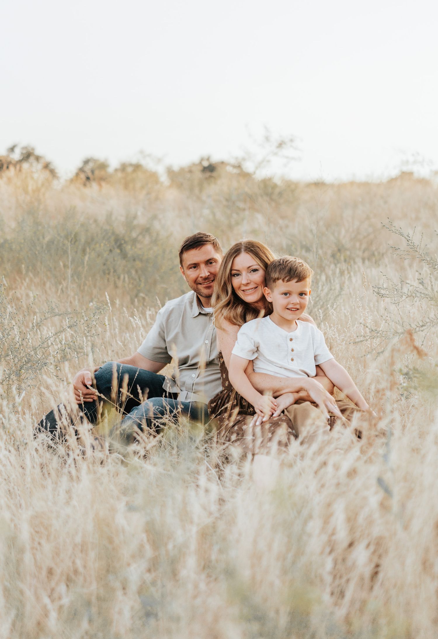 A beautiful family portrait taken in a serene field of dried grass during golden hour.