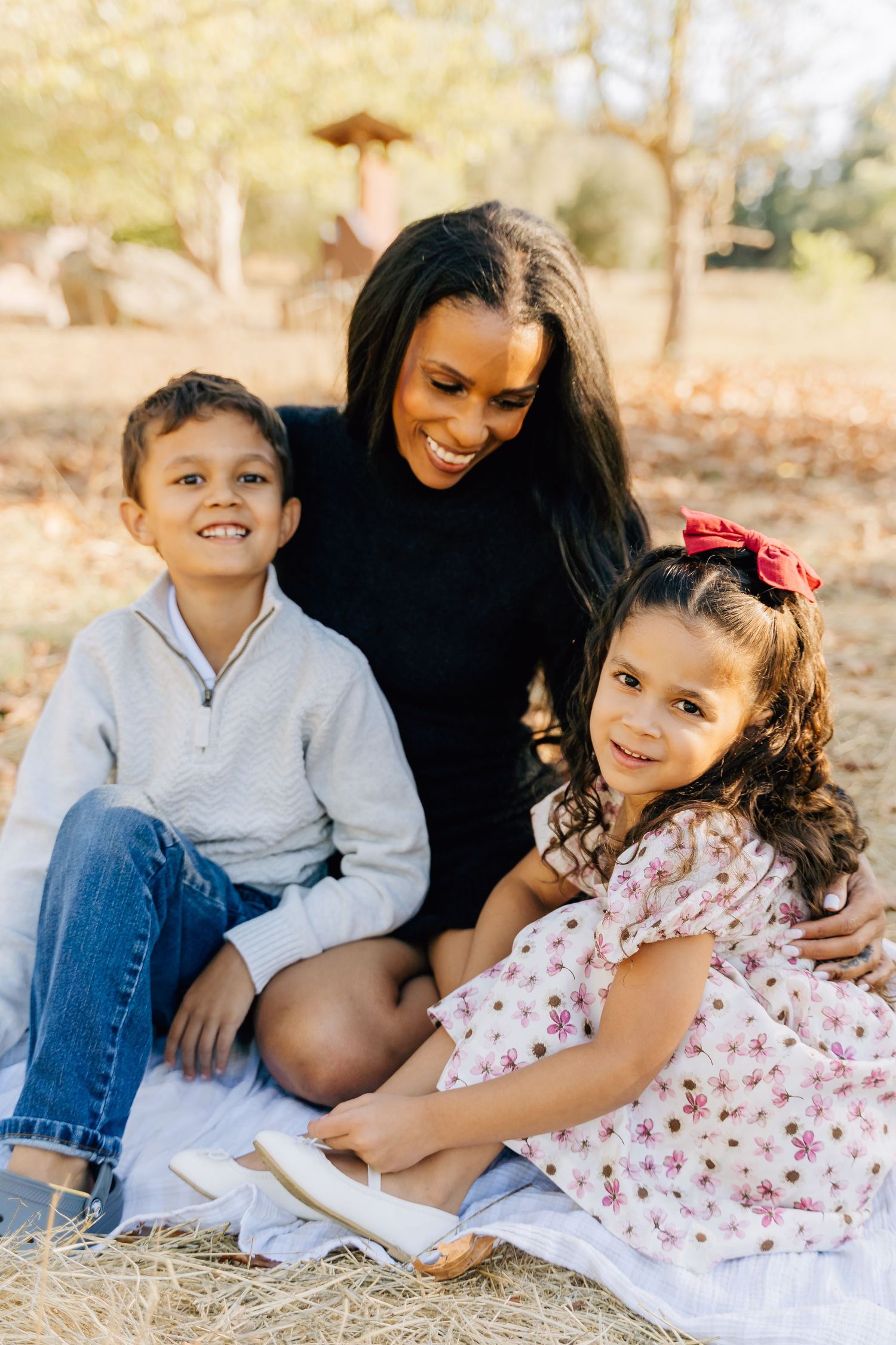 A joyful outdoor portrait of a mother sitting with her two children on a blanket during autumn.